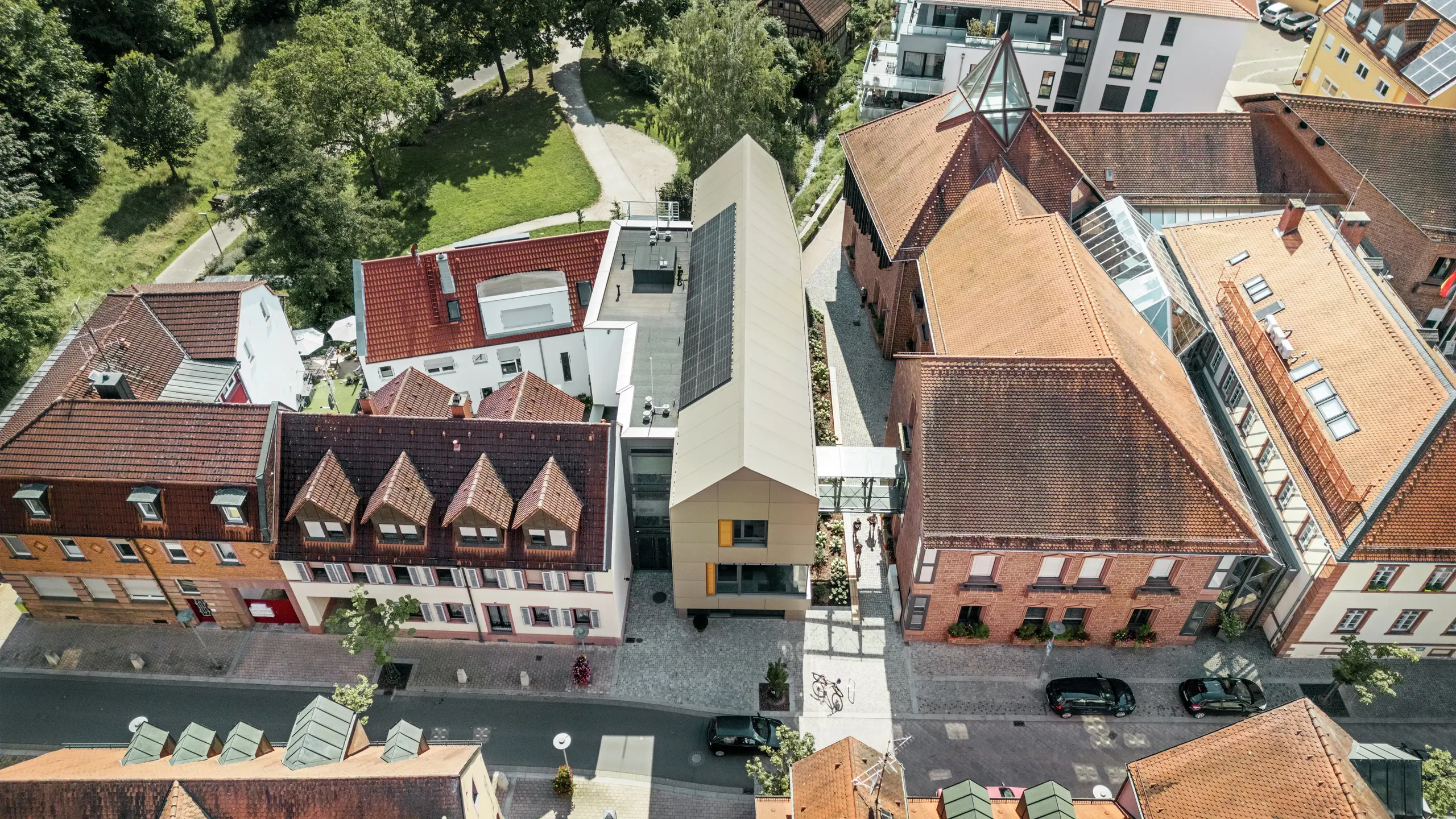 Gradska vijećnica u Alzenauu, Njemačka, nalazi se u središtu povijesnog gradskog okruženja, okružena tradicionalnim zgradama s crvenim crijepnim krovovima. U kontrastu s tim stoji moderna gradska vijećnica čija je fasada obložena aluminijskim kompozitnim pločama PREFA u elegantnoj brončanoj boji. Inovativna arhitektura jasno se izdvaja od susjednih klasičnih zgrada, a istovremeno se skladno uklapa u gradski pejzaž.
