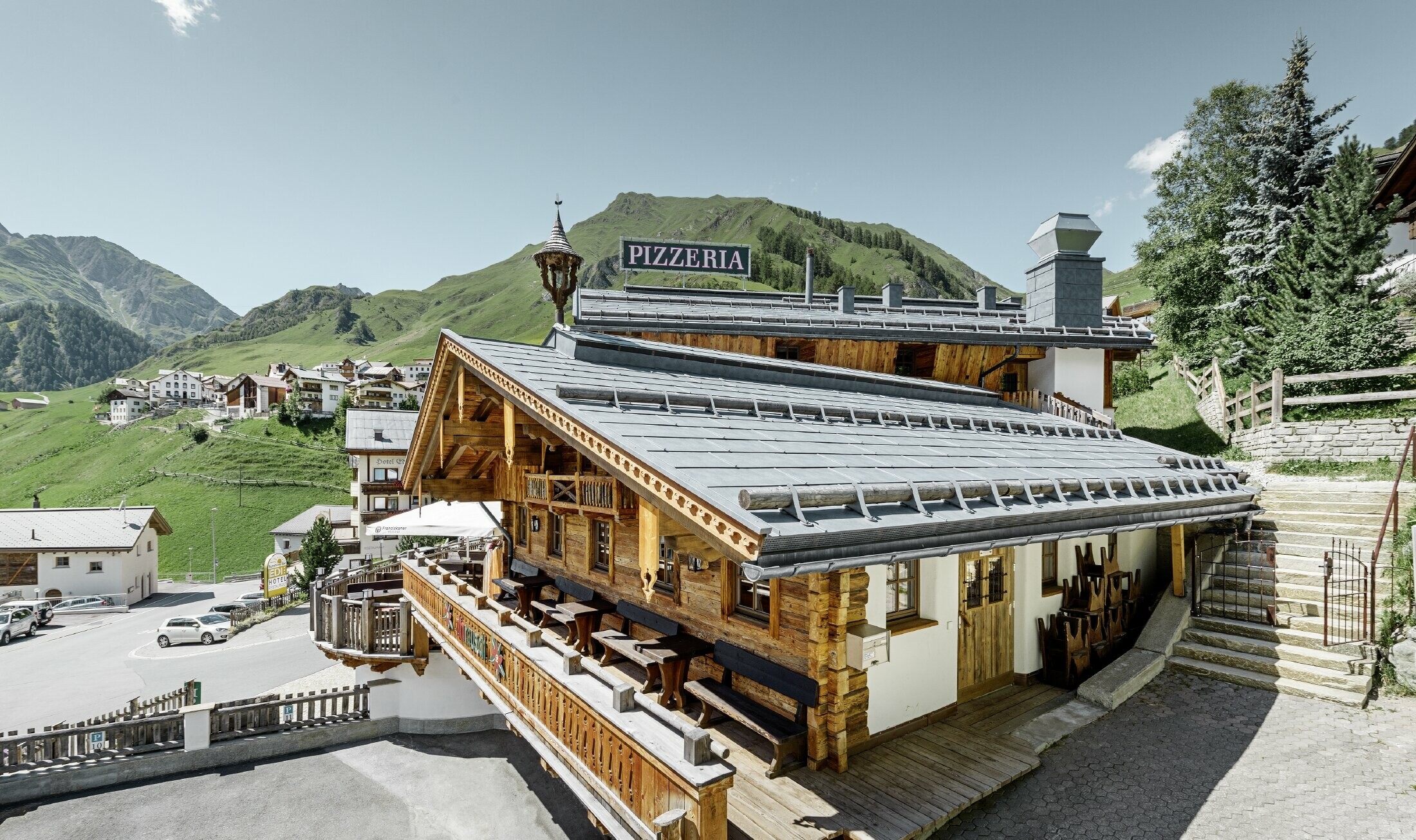Restoran Almrausch s brdima u pozadini i PREFA krovom pokrivenim krovnim panelom FX.12 u kameno sivoj boji s planinskim snjegobranima