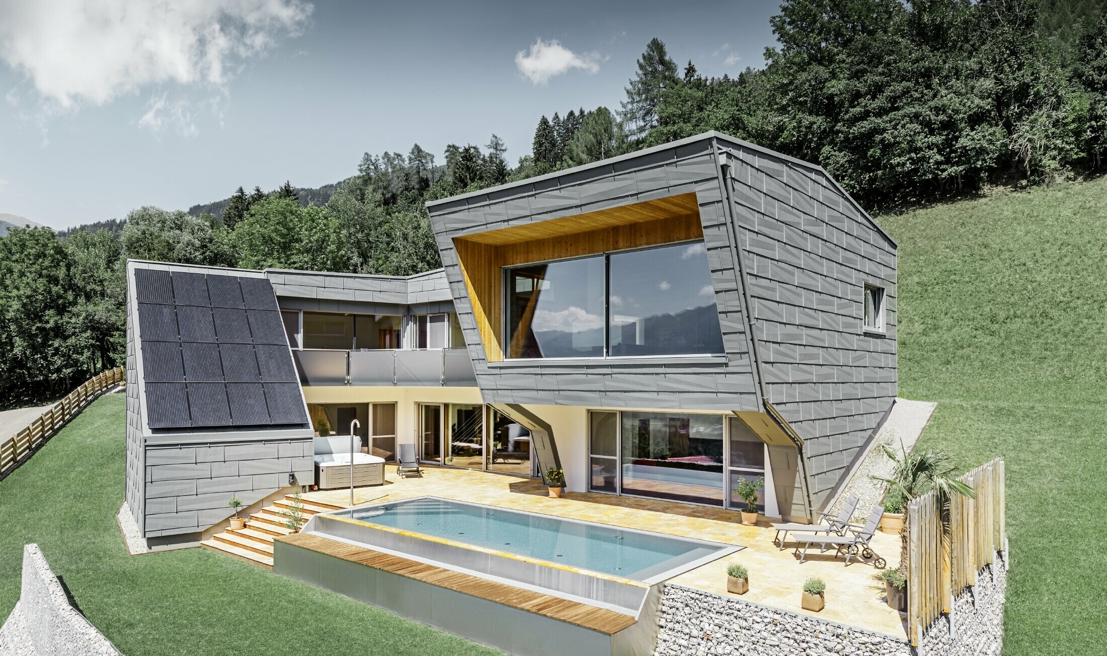 Moderna obiteljska kuća na padini s bazenom obložena je fasadnim panelom FX.12 tvrtke PREFA u P.10 svijetlo sivoj.