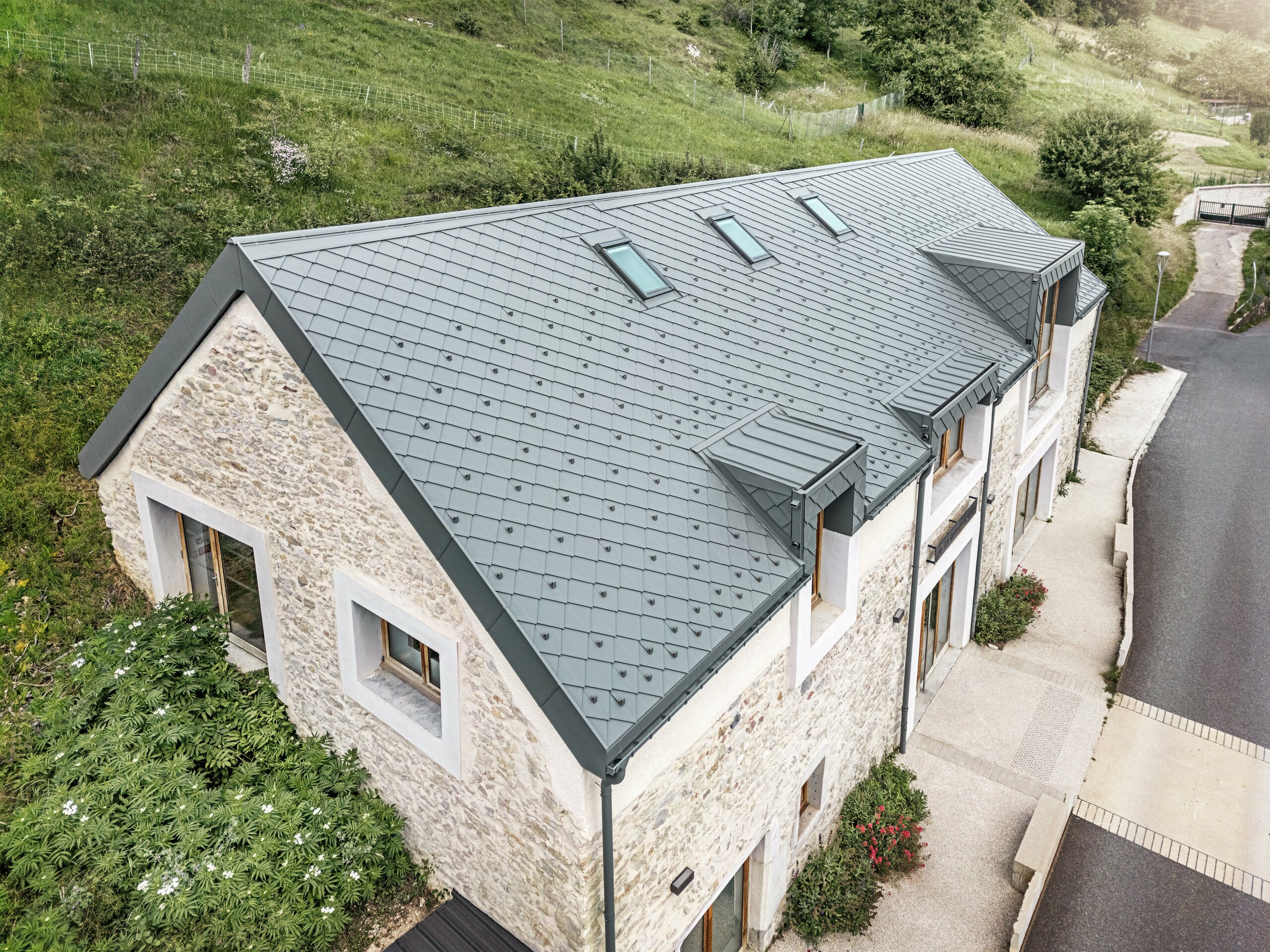 Pogled na krov obnovljene štale "La Grange à Gaby" u Enginsu, Francuska. Moderni PREFA aluminijski krov s rombovima veličine 29 × 29 cm skladno se uklapa u povijesnu kamenu građevinu i pruža dugotrajnu zaštitu od vremenskih utjecaja.