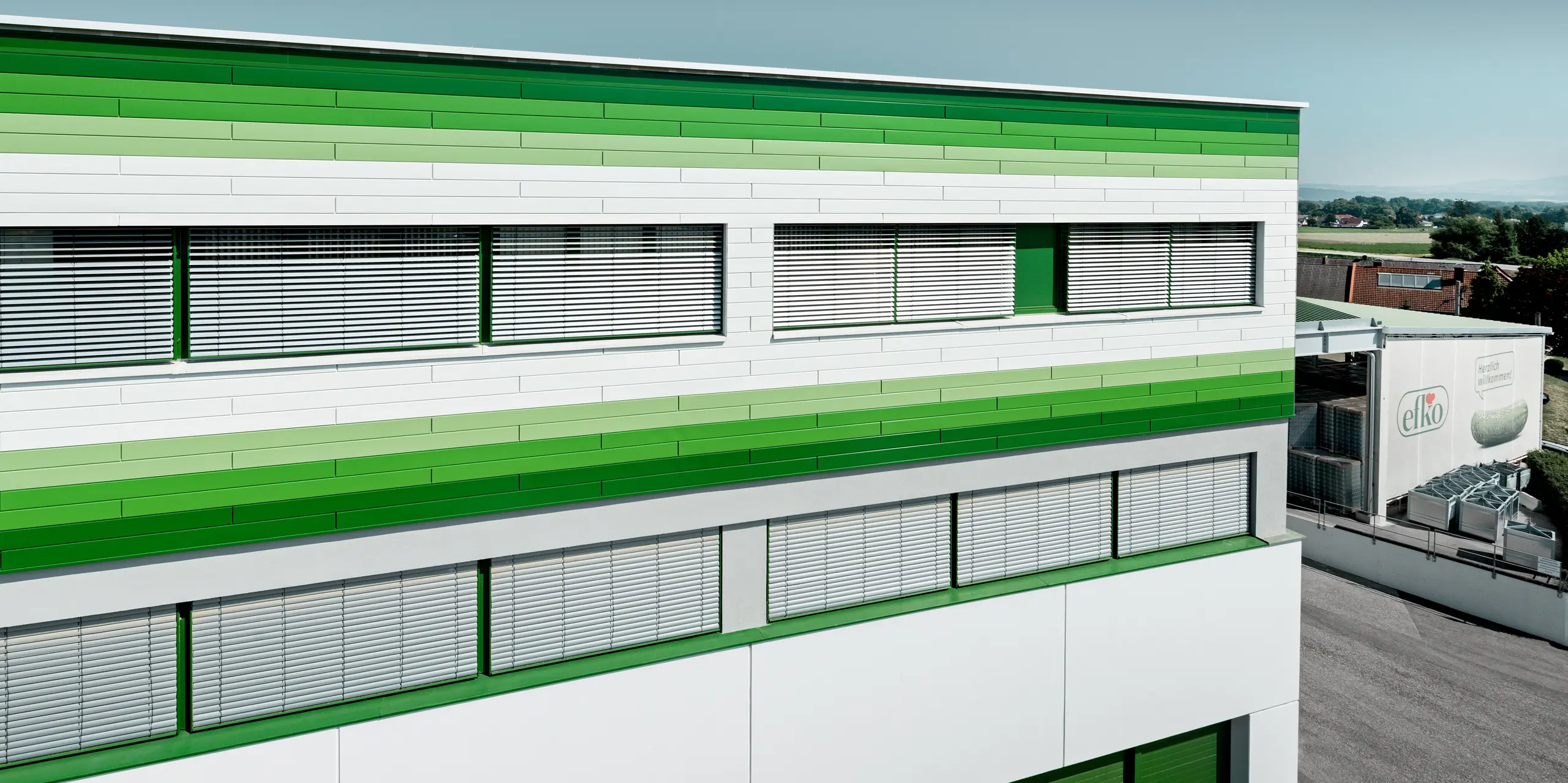 Die moderne Fassade des efko Firmengebäudes setzt mit PREFA Sidings in P.10 Prefaweiß und abgestuften grünen RAL-Sonderbeschichtungen markante Akzente. Die horizontalen Linien unterstreichen die großzügige Architektur und schaffen ein dynamisches Fassadenbild. Die hochwertigen PREFA Aluminiumprodukte überzeugen durch Langlebigkeit, Witterungsbeständigkeit, Farbstabilität und einen geringen Wartungsaufwand bei dauerhaft ansprechender Optik.