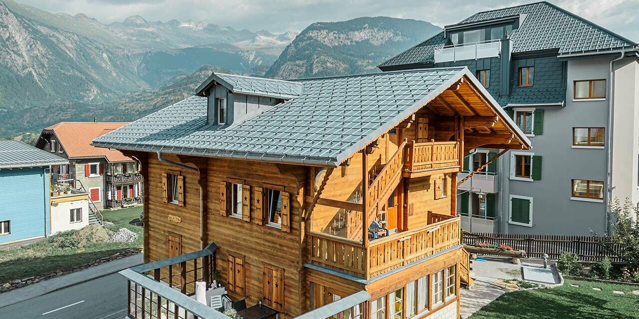 Tradicionalna drvena švicarska kuća s krovnom kućicom i dvostrešnim krovom; Krov je pokriven klasičnim PREFA krovnim pločama u kameno sivoj.