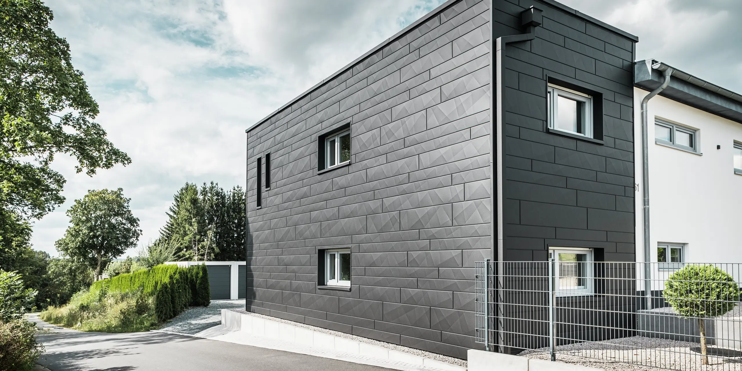 Die Rückseite des modernisierten Einfamilienhauses in Teuschnitz beeindruckt mit einer eleganten Fassade aus PREFA Siding.X in der Farbe P.10 Schwarz. Die geometrischen Blechpaneele erzeugen eine markante, strukturierte Optik und verleihen dem Gebäude einen modernen und zeitlosen Charakter. Die integrierte PREFA Dachentwässerung mit Quadratrohr und Wasserfangkasten fügt sich harmonisch in das Gesamtbild ein und verbindet Ästhetik mit Funktionalität.