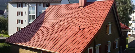 Dvostrešni krov pokriven PREFA krovnom pločom od aluminija. Krov u ciglasto crvenoj boji sa snjegobranima i dimnjakom