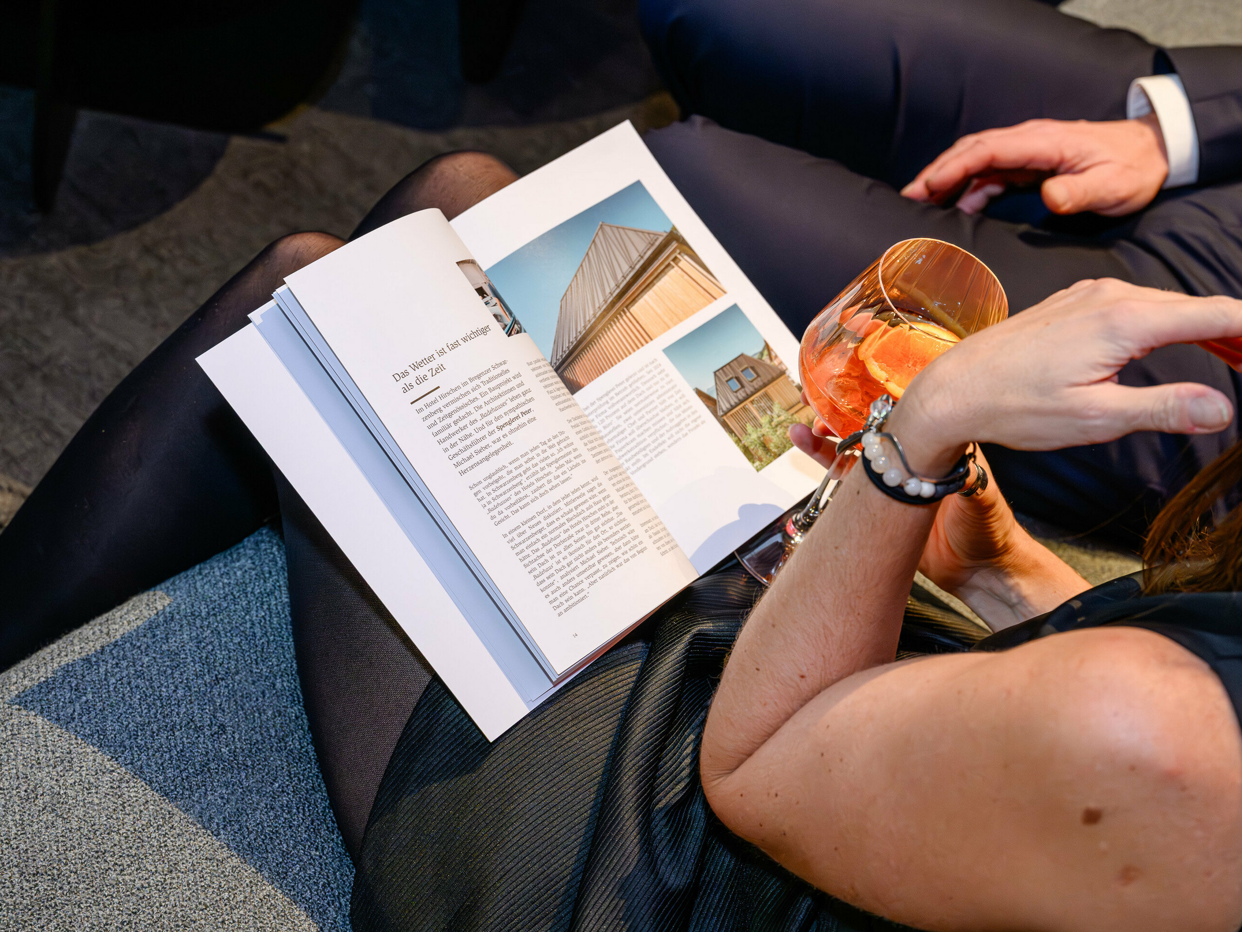 Atmosferična scena na PREFARENZEN prezentaciji 2026. u K47.wien: elegantna dama prelistava novu PREFA arhitektonsku knjigu držeći piće u ruci – pravi vizualni fokus pun inspiracije za dizajn. Vidljiv je objekt s PREFALZ krovnim pokrovom koji impresionira modernim aluminijskim karakterom. Fotografija prenosi užitak, razmjenu iskustava i znatiželju za inovacijama. Kvalitetna PREFA površina spaja estetiku i dugotrajnost – savršeno za kreativne arhitektonske ideje. PREFA aluminij postavlja standarde i oduševljava profesionalce, planere, arhitekte i izvođače podjednako.