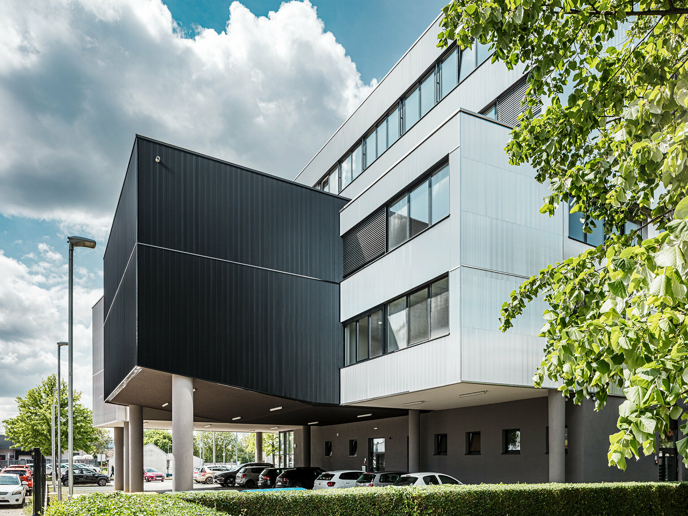 Moderna poslovna zgrada Glazbene škole Bjelovar u Hrvatskoj ističe se upečatljivom aluminijskom fasadom od PREFA zubčastih ekstruzijskih profila. Fasadne površine eloksirane u crnoj i srebrnoj boji stvaraju jasne arhitektonske kontraste i daju zgradi karakter i dubinu. Vertikalno postavljeni profili oblikuju elegantnu strukturu s zanimljivom igrom svjetla i sjene. Zahvaljujući robusnoj, otpornom na koroziju aluminijskoj površini, fasadni elementi su iznimno dugotrajni i jednostavni za održavanje. Nevidljivo pričvršćivanje osigurava ravnomjeran i visokokvalitetan izgled. Ova predmontirana, ventilirana PREFA-fasada spaja dizajn, tehnologiju i funkcionalnost.