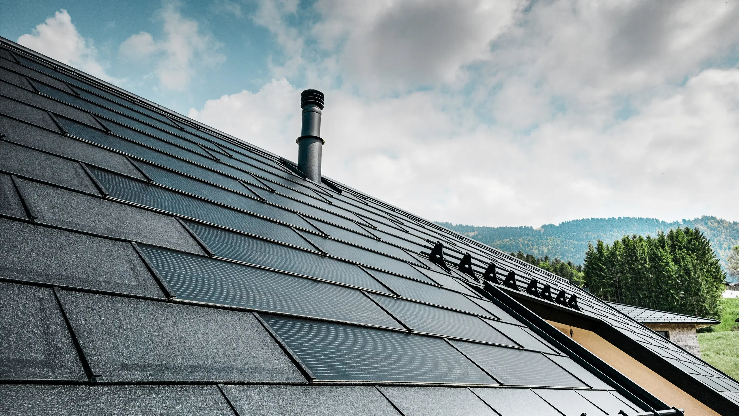 Detaljan prikaz PREFA solarne krovne ploče u kombinaciji s dokazanom PREFA krovnom pločom R.16 u boji P.10 Black na eko-kući u Eggu, Austrija. Integrirani fotonaponski moduli pokazuju besprijekornu vezu obnovljive energije i sofisticiranog dizajna krova. Crni krovni paneli R.16 sa sustavom zaštite od snijega zaokružuju estetsku površinu krova i osiguravaju sigurnost.
