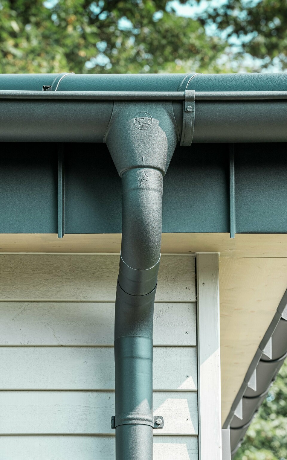 Nahaufnahme der robusten PREFA Dachentwässerung eines Bungalows in Rommerskirchen. Die hochwertige Saumrinne und das Ablaufrohr in P.10 Schwarz bieten optimalen Schutz vor Witterungseinflüssen. Langlebigkeit und Funktionalität verbinden sich hier mit elegantem Design aus Aluminium.