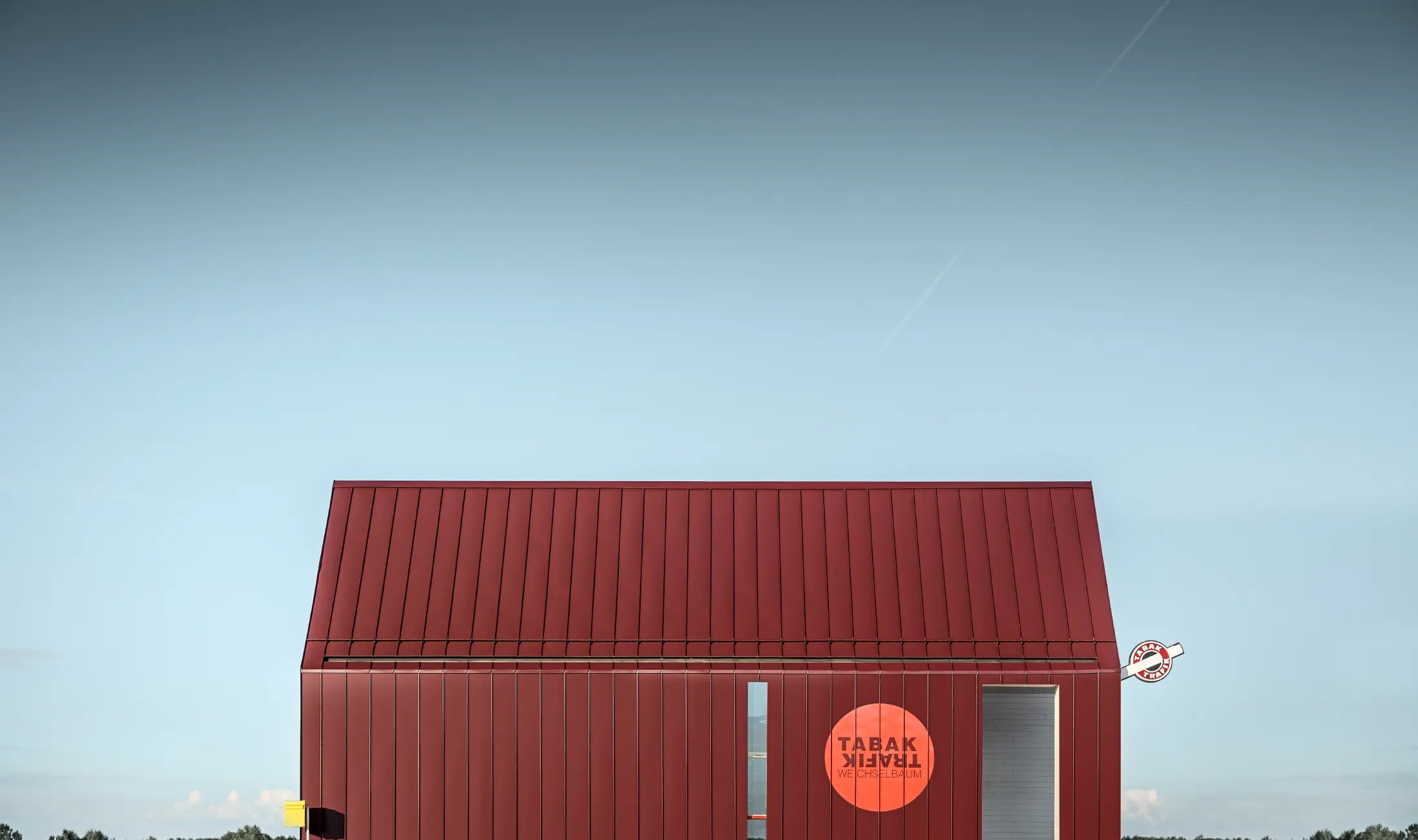Moderni kiosk s dvostrešnim krovom bez streha, izveden s aluminijskom oblogom od PREFE sa stojećim falcom i kutnim stojećim falcom u specijalnoj crno crvenoj boji