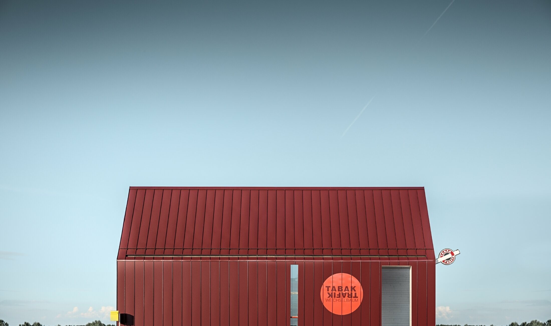 Moderni kiosk s dvostrešnim krovom bez streha, izveden s aluminijskom oblogom od PREFE sa stojećim falcom i kutnim stojećim falcom u specijalnoj crno crvenoj boji