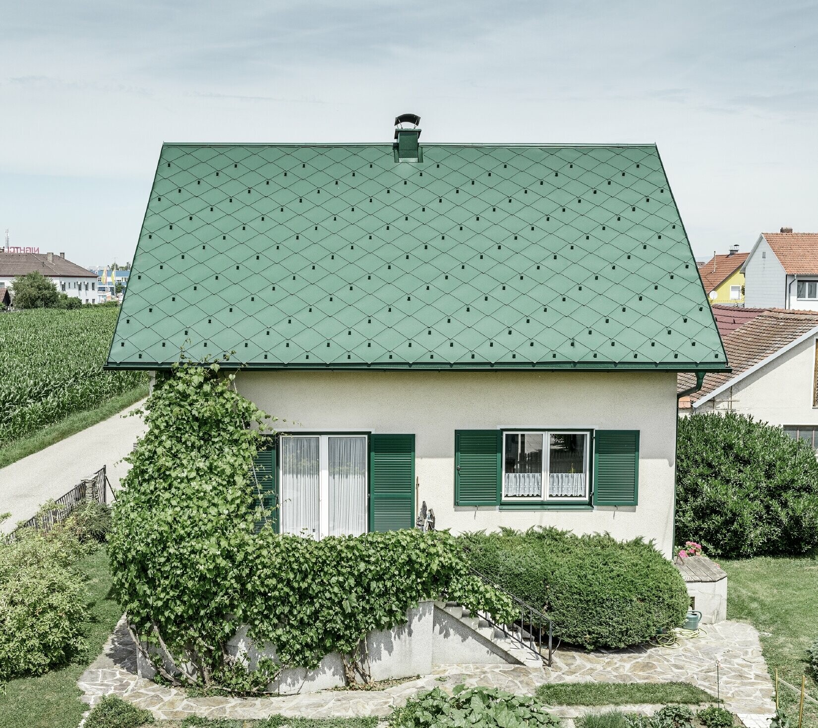Klasična jednoobiteljska kuća s dvostrešnim krovom s krovnim pokrovom od aluminija u mahovinasto zelenoj boji sa zelenim prozorskim kapcima. Krov je pokriven PREFA krovnim rombovima 44 × 44 u P.10 mahovinasto zelenoj boji.
