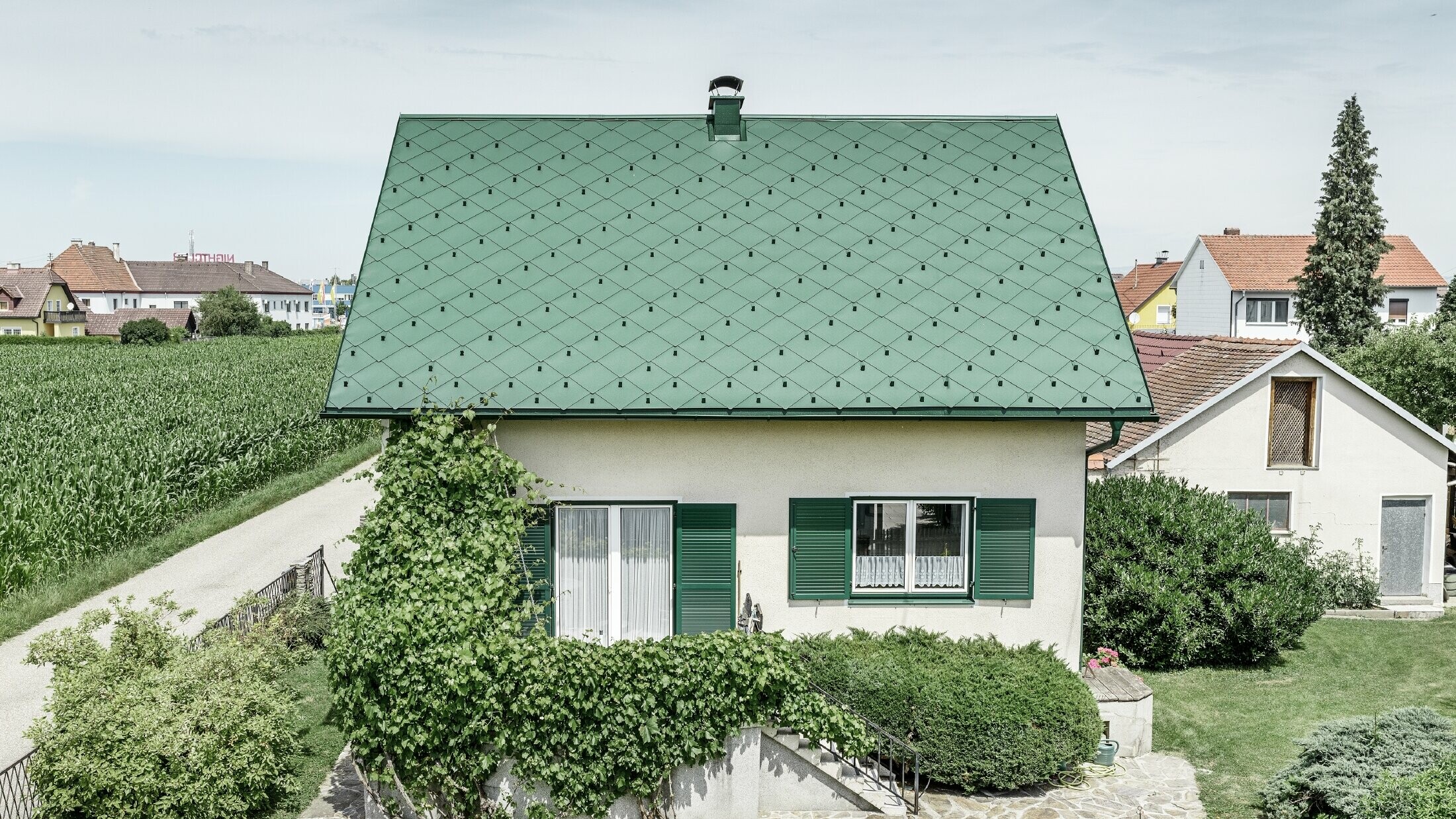 Klasična jednoobiteljska kuća s dvostrešnim krovom s krovnim pokrovom od aluminija u mahovinasto zelenoj boji sa zelenim prozorskim kapcima. Krov je pokriven PREFA krovnim rombovima 44 × 44 u P.10 mahovinasto zelenoj boji.