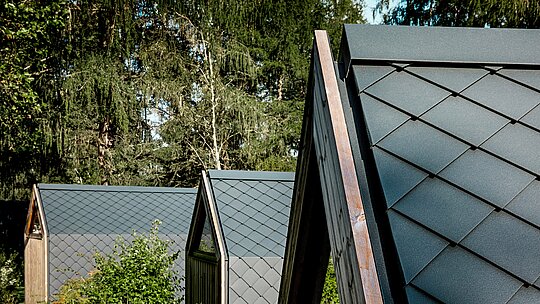 Nekoliko minimalističkih A-Frame tiny kuća Secret Koi Gardena skladno je poredano uz rub šume na jezeru Natterer See. Krovne površine obložene su sitnim PREFA aluminijskim rombovima u P.10 antracitnoj boji, koji stvaraju upečatljivu strukturu nalik ribljoj koži.  Matirana površina djeluje smireno i elegantno, dok dugotrajni i vremenski otporni PREFA aluminij pruža optimalnu zaštitu u alpskom okruženju te savršeno povezuje dizajn i prirodu.