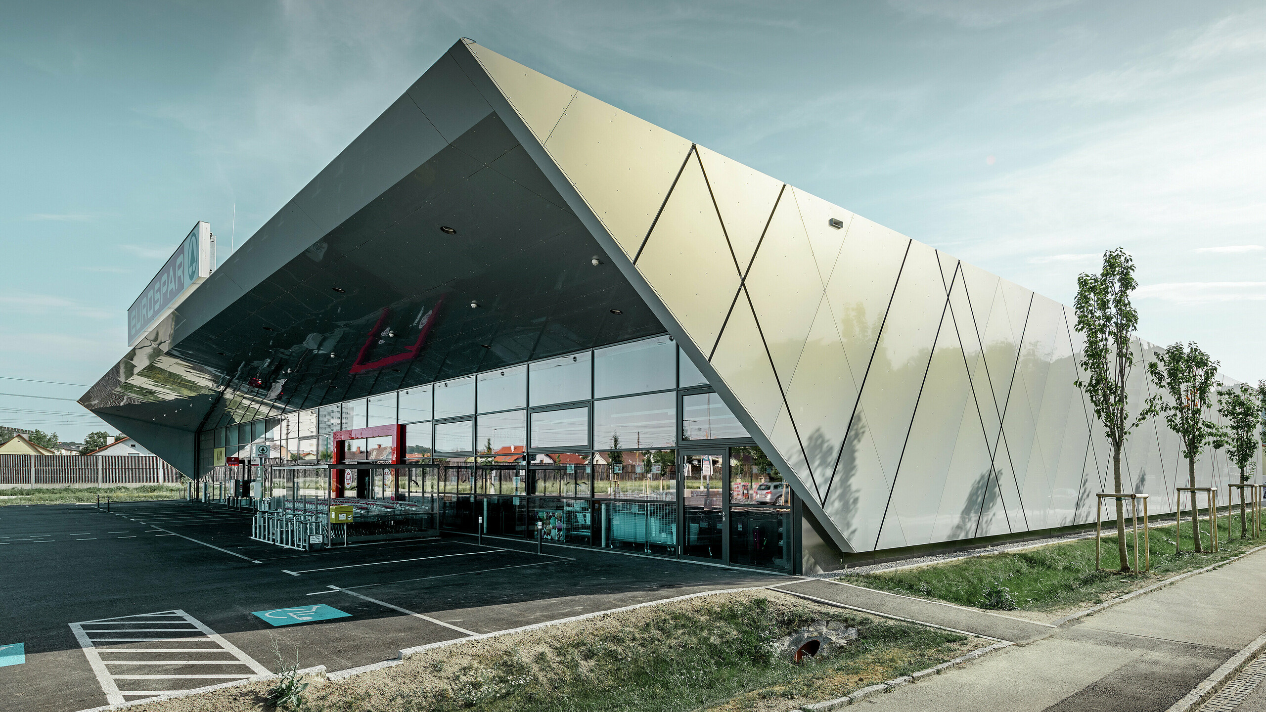 Područje ulaza nove podružnice Eurospara u Welsu s modernom fasadnom pločom tvrtke PREFA u srebrno zlatnoj; Aluminijske kompozitne ploče se, ovisno o kutu gledanja, prelijevaju na suncu u različitim bojama.
