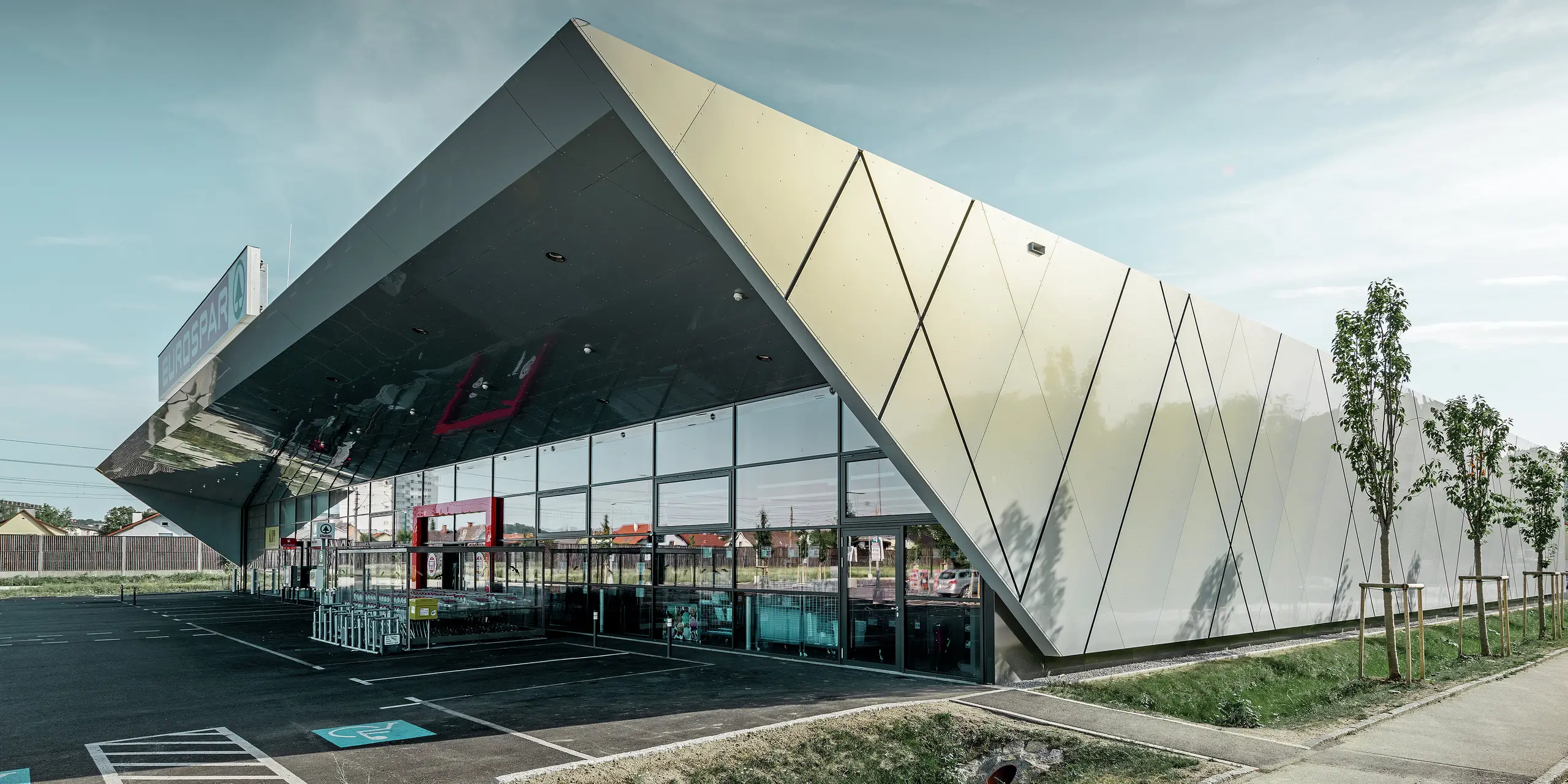 Područje ulaza nove podružnice Eurospara u Welsu s modernom fasadnom pločom tvrtke PREFA u srebrno zlatnoj; Aluminijske kompozitne ploče se, ovisno o kutu gledanja, prelijevaju na suncu u različitim bojama.