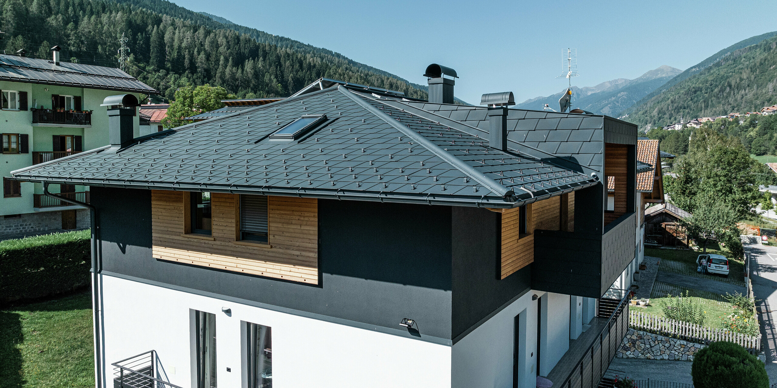 Blick auf das Dachgeschoss des Wohnhauses in Commezzadura mit PREFA Dachschindeln DS.19 in P.10 Anthrazit und Holzfassade. Das hochwertige Blechdach schützt das Gebäude vor den alpinen Witterungsbedingungen.