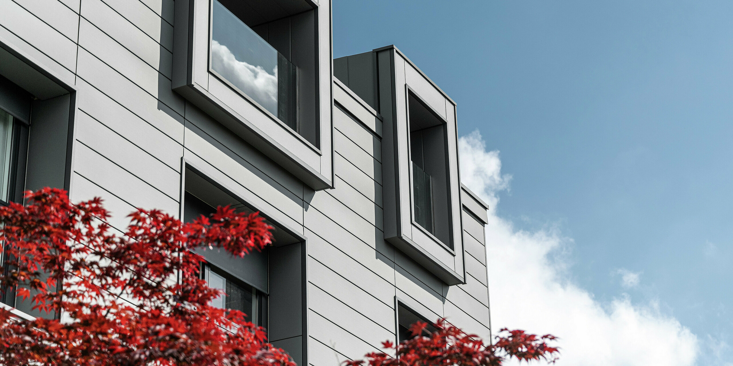 Moderne Wohnanlage in Faloppio, Italien, mit auskragenden Fenstern und einer eleganten Fassade aus PREFA Sidings. Die Aluminiumverkleidung sorgt für eine stilvolle Optik und bietet gleichzeitig hohe Widerstandsfähigkeit und Langlebigkeit. Ein gelungenes Beispiel für funktionelle Architektur mit hochwertigen PREFA Produkten.
