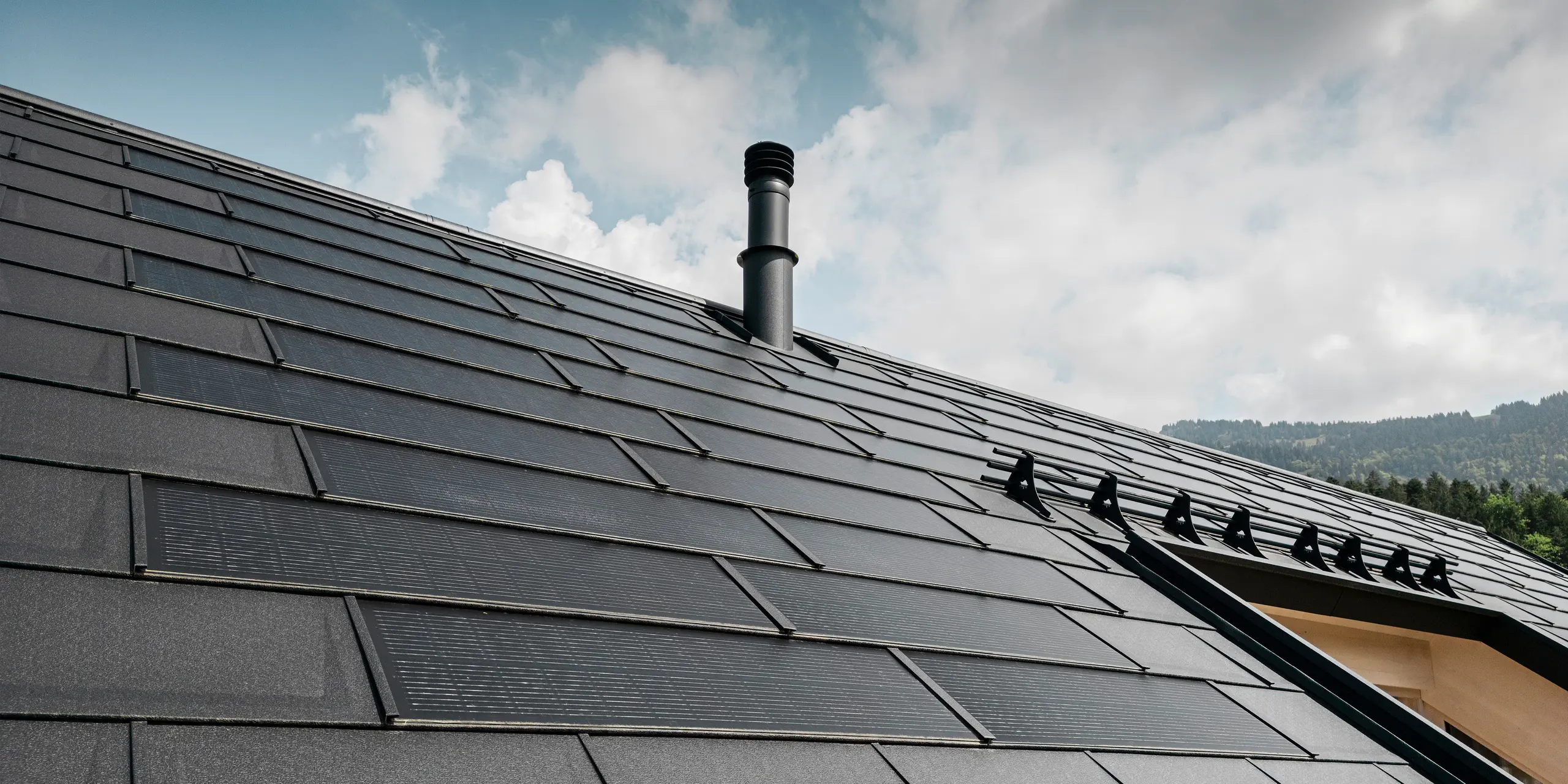 Krupni kadar učinkovite PREFA solarne krovne ploče koja se besprijekorno uklapa u crni krov od robusnih PREFA krovnih ploča R.16. Kombinacija održive proizvodnje energije i dugotrajnog aluminijskog krova nudi ekološko i estetsko rješenje za krov koje se skladno uklapa u prirodni krajolik.