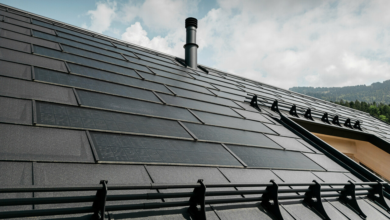 Krupni kadar učinkovite PREFA solarne krovne ploče koja se besprijekorno uklapa u crni krov od robusnih PREFA krovnih ploča R.16. Kombinacija održive proizvodnje energije i dugotrajnog aluminijskog krova nudi ekološko i estetsko rješenje za krov koje se skladno uklapa u prirodni krajolik.
