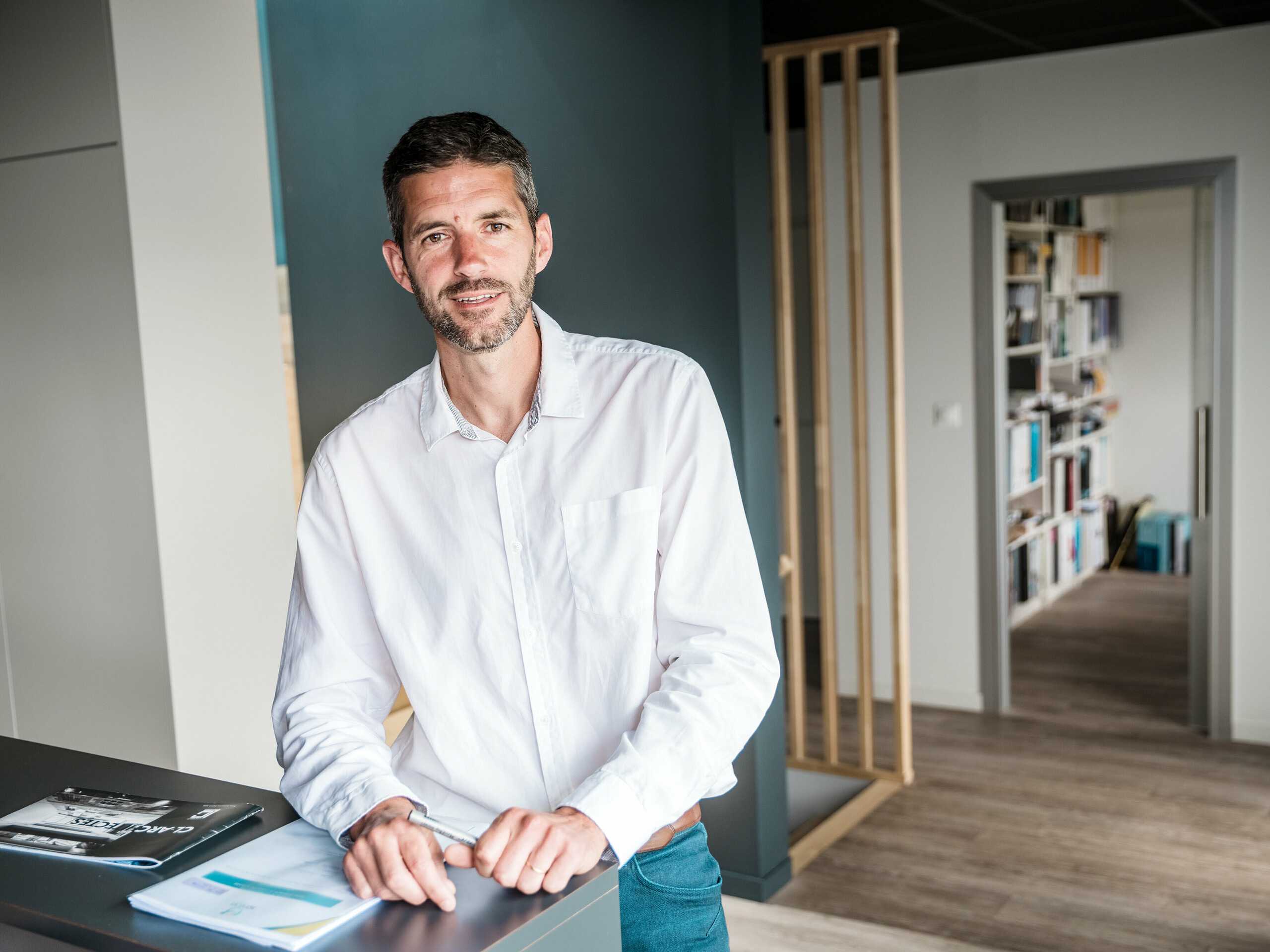 U prvom planu fotografije nalazi se arhitekt Hugues Launay iz arhitektonske tvrtke CLARC Architectes. Muškarac je smješten u središtu, odnosno malo ulijevo, i nosi formalnu odjeću, primjerenu profesionalnom intervjuu. U pozadini se vidi zakrivljena aluminijska fasada Collège Léontine Dolivet, čija srebrno-metalna površina stvara refleksije svjetla. Osoba gleda blago bočno, a držanje tijela djeluje prisutno i samouvjereno, što sugerira ulogu odgovorne osobe za projekt. Scena je snimljena danju, s mekanim prirodnim svjetlom koje jasno ističe konture.