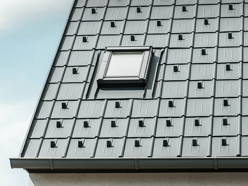 PREFA krovna ploča s protivsnježnim elementima u antracit boji postavljena s ugrađenim krovnim prozorom i PREFA olucima. Krovna površina s PREFA limenim krovom.