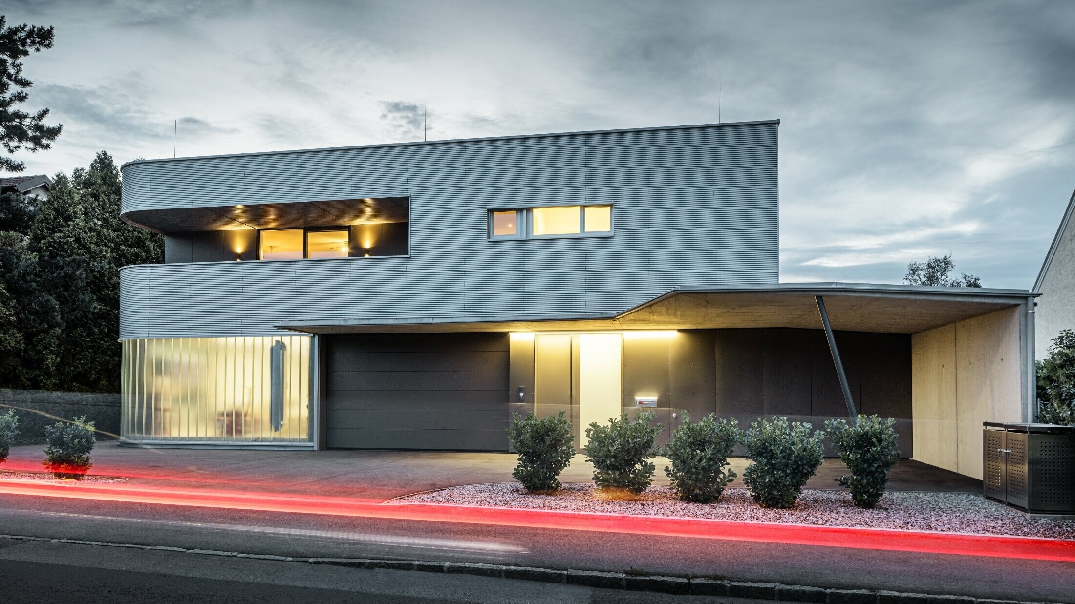 Moderna stambena kuća s fasadom u natur boji od PREFA valovitog profila s garažom, fotografirano pri večernjem svjetlu