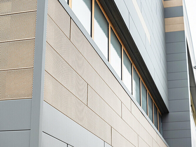 Fasadni paneli tvrtke PREFA, fasadna kazeta, dostupni su sada i u perforiranoj, dakle izbušenoj izvedbi, ovdje su kombinirani pješčanosmeđi probušeni elementi sa sivim panelima. 