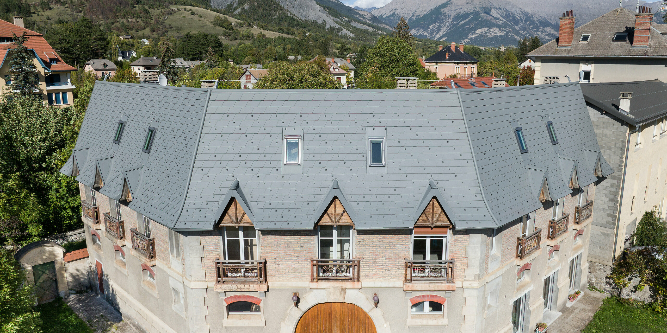 Frontansicht eines Anwesens in Barcelonnette, Frankreich. Das großflächige Dach wurde mit der PREFA Dachschindel in P.10 Hellgrau saniert. 