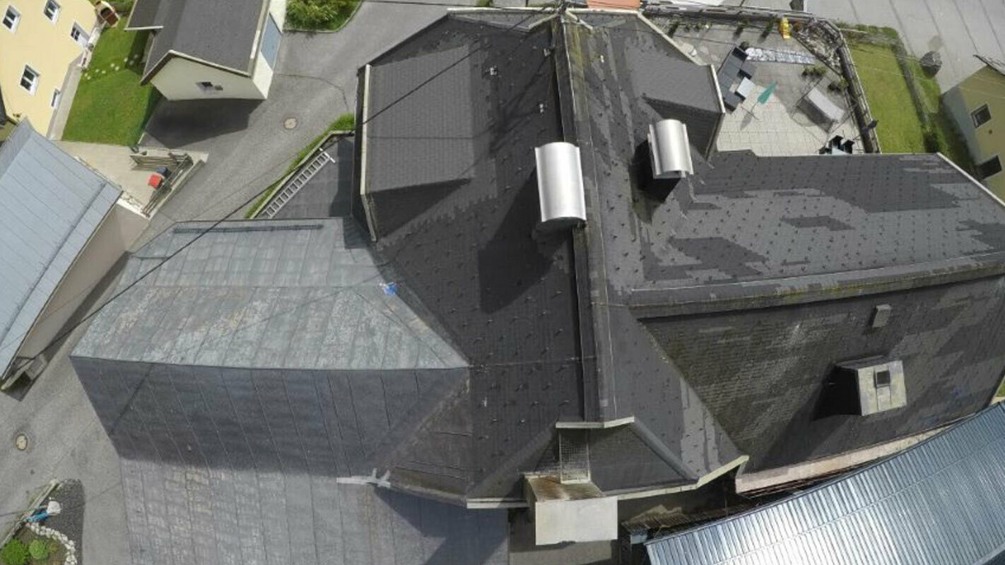 Ptičja perspektiva starog krova s puno detalja - s uvalama, krovnim kućicama i dimnjacima. Stari krovni pokrivač više je puta popravljan i pokriven mrljama.