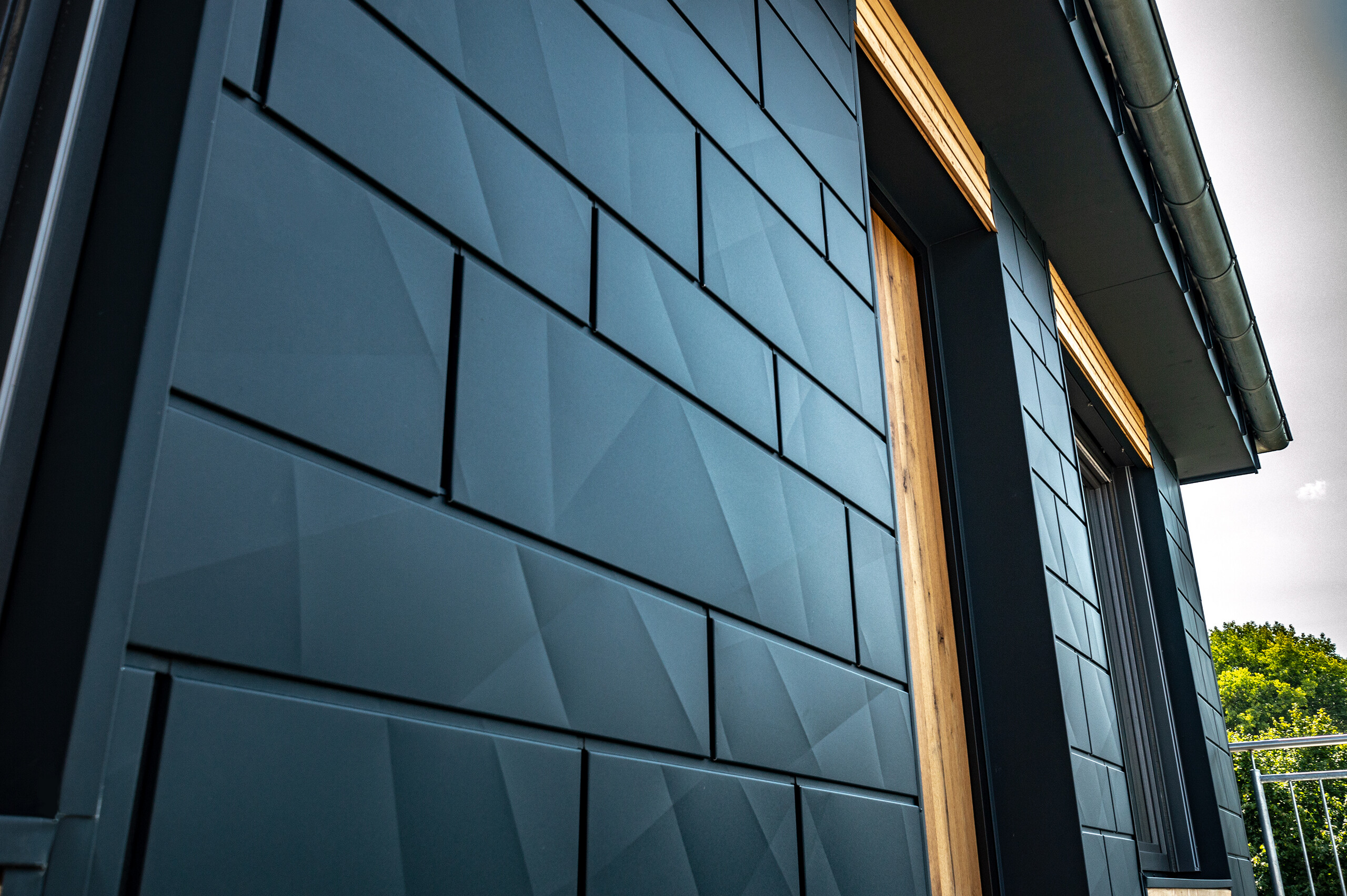 Fasada s PREFA fasadnom kazetom.X u antracit boji s balkonskim vratima i velikim staklenim površinama, u kombinaciji s drvenom fasadom.