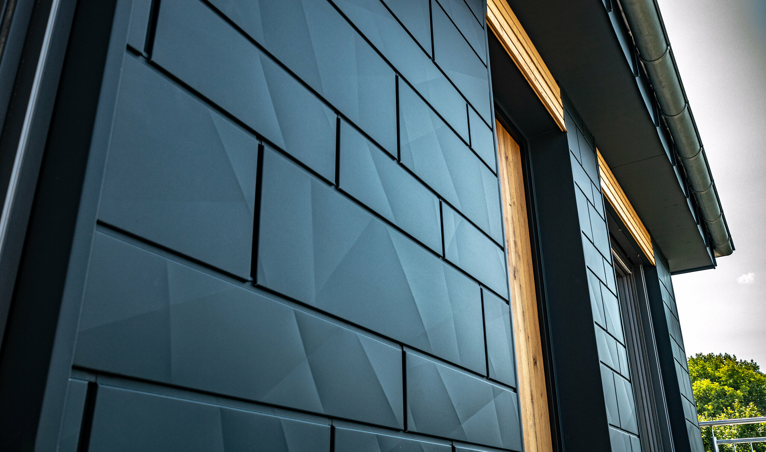 Fasada s PREFA fasadnom kazetom.X u antracit boji s balkonskim vratima i velikim staklenim površinama, u kombinaciji s drvenom fasadom.