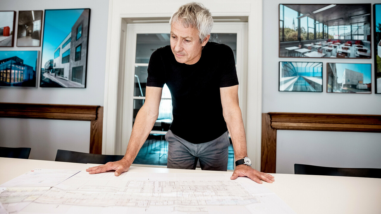 Arhitekt radi na detaljnim nacrtima zgrade u modernom uredu, okružen impresivnim fotografijama PREFA arhitektonskih projekata.