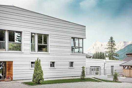 Detaljan prikaz vojarne „Tempesti“ s precizno postavljenim PREFALZ panelima u boji P.10 Prefaweiß. Jasne linije horizontalno postavljene falcane obloge naglašavaju moderan dizajn fasade. Svijetla površina reflektira sunčevu svjetlost i optimizira mikroklimu. U pozadini se uzdiže impresivan planinski pejzaž Južnog Tirola – ovdje se tehnologija susreće s prirodom na najvišoj razini.