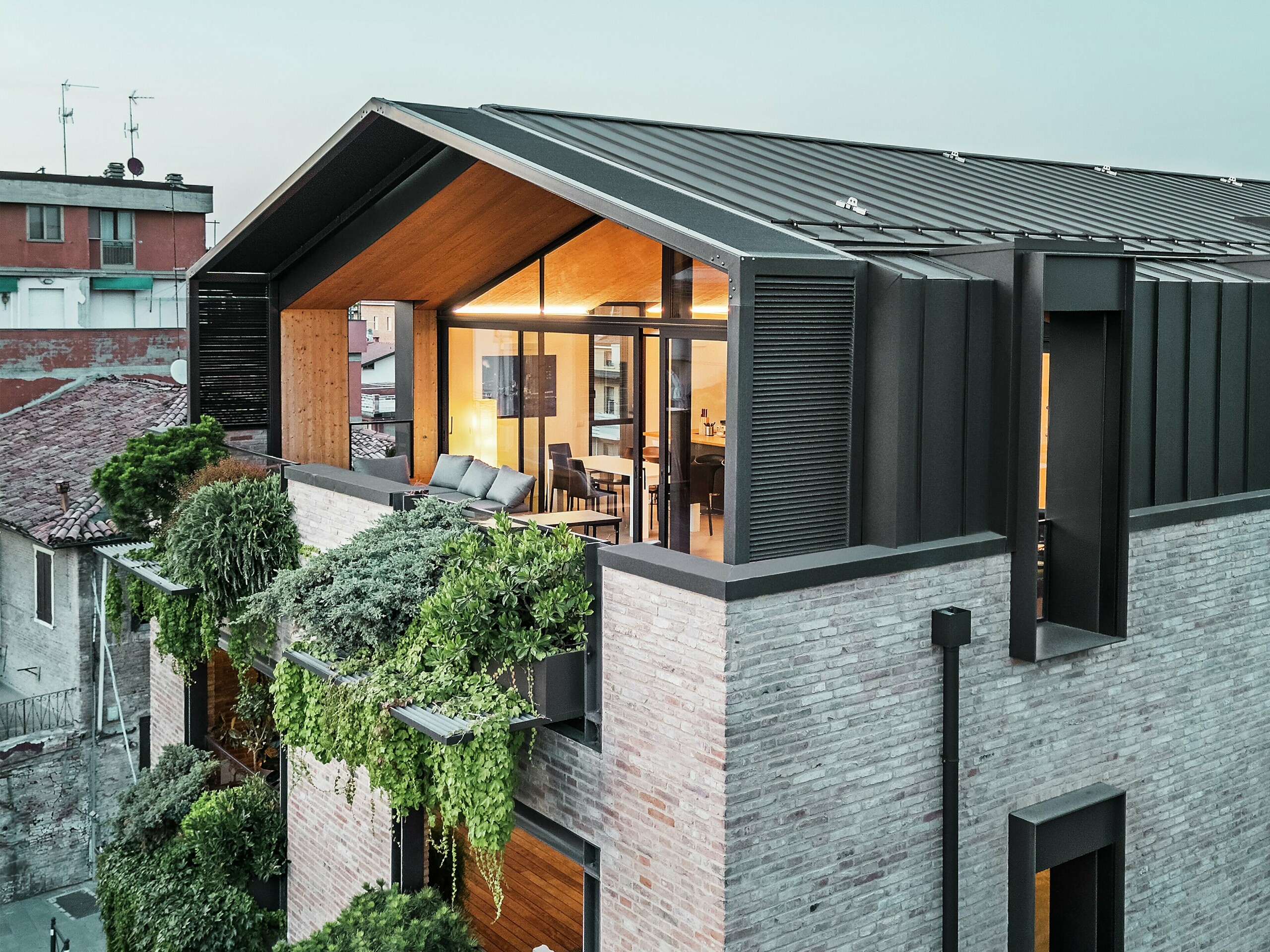 Moderna stambena kuća u Italiji s PREFALZ aluminijskim krovom u boji P.10 smeđa lješnjaka, velikim staklenim površinama, ozelenjenom fasadom i opekom – uspješna kombinacija održivosti i suvremene arhitekture.