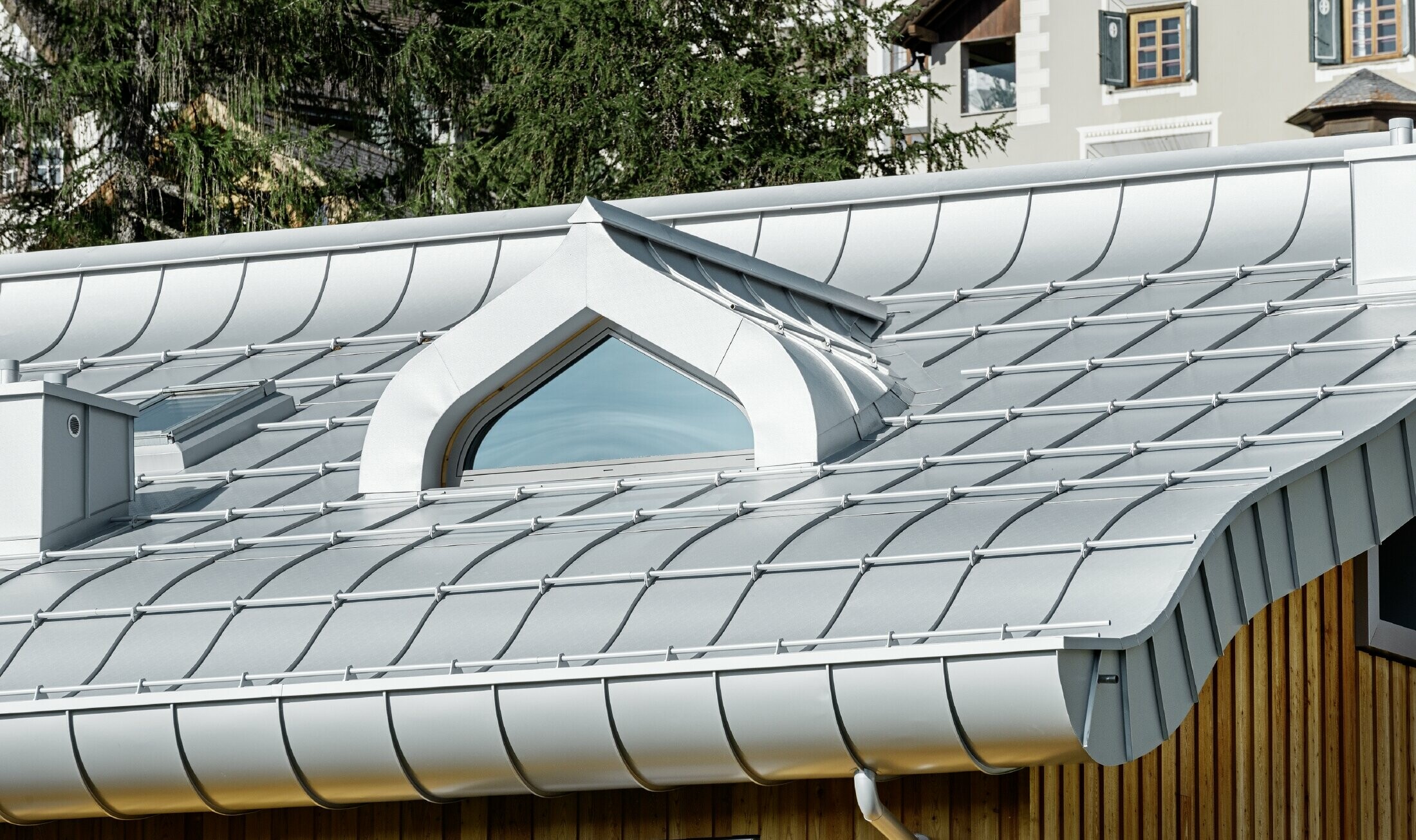 Stambeno naselje u St. Moritzu s drvenom fasadom i aluminijskim krovom s lučnom strehom u srebrnoj metalik boji