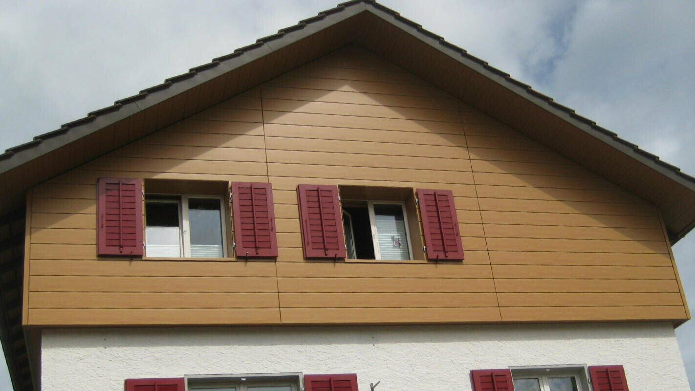 Fasada kuće u optici drva s PREFA fasadnim kazetama Siding horizontalno položenim, prozori s crvenim griljama