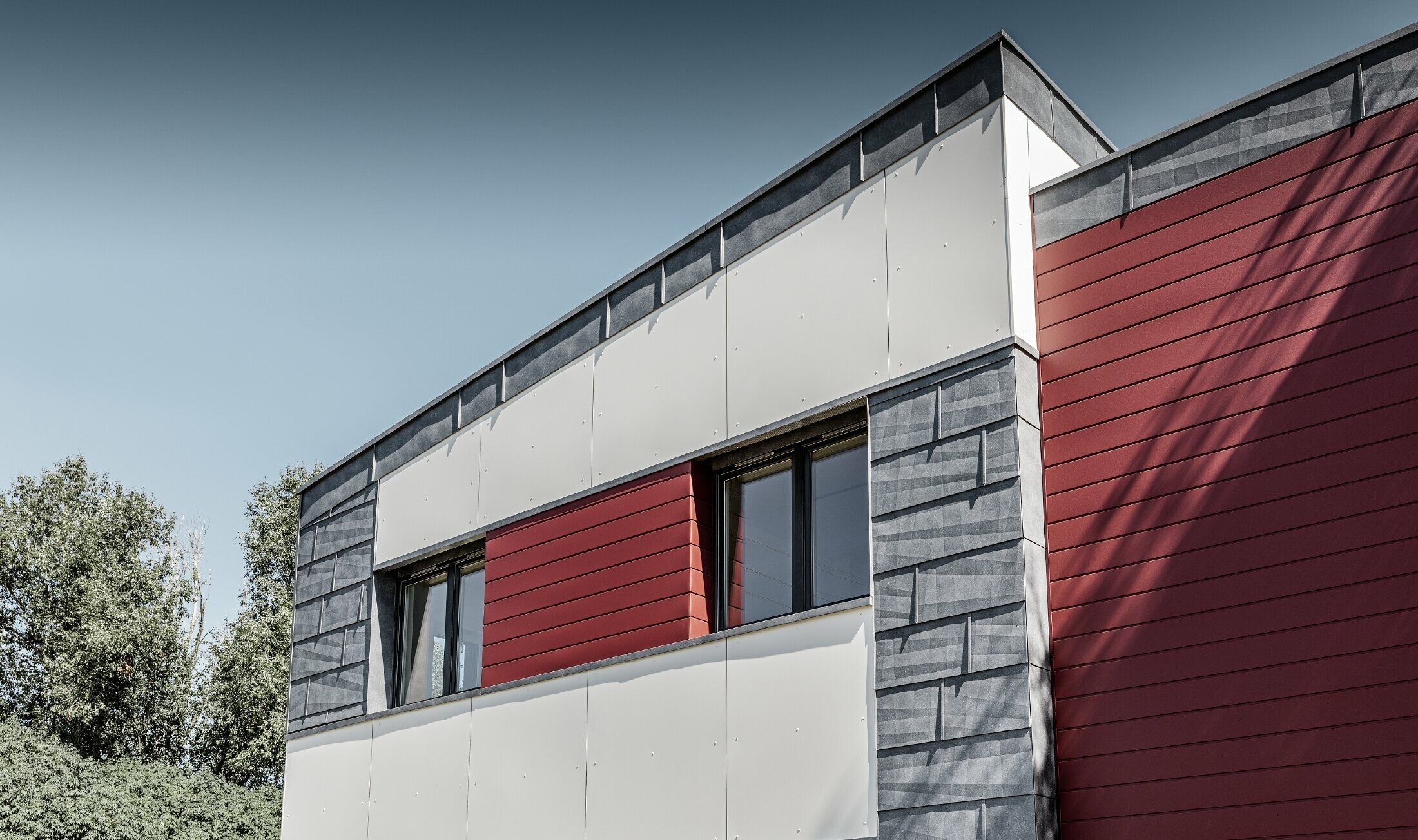 Moderna uredska zgrada s višedjelnom fasadom u crvenoj, kameno sivoj i bijeloj boji, s aluminijskim proizvodima fasadnim kazetama, fasadnim panelom FX.12 i aluminijskom kompozitnom pločom od PREFE