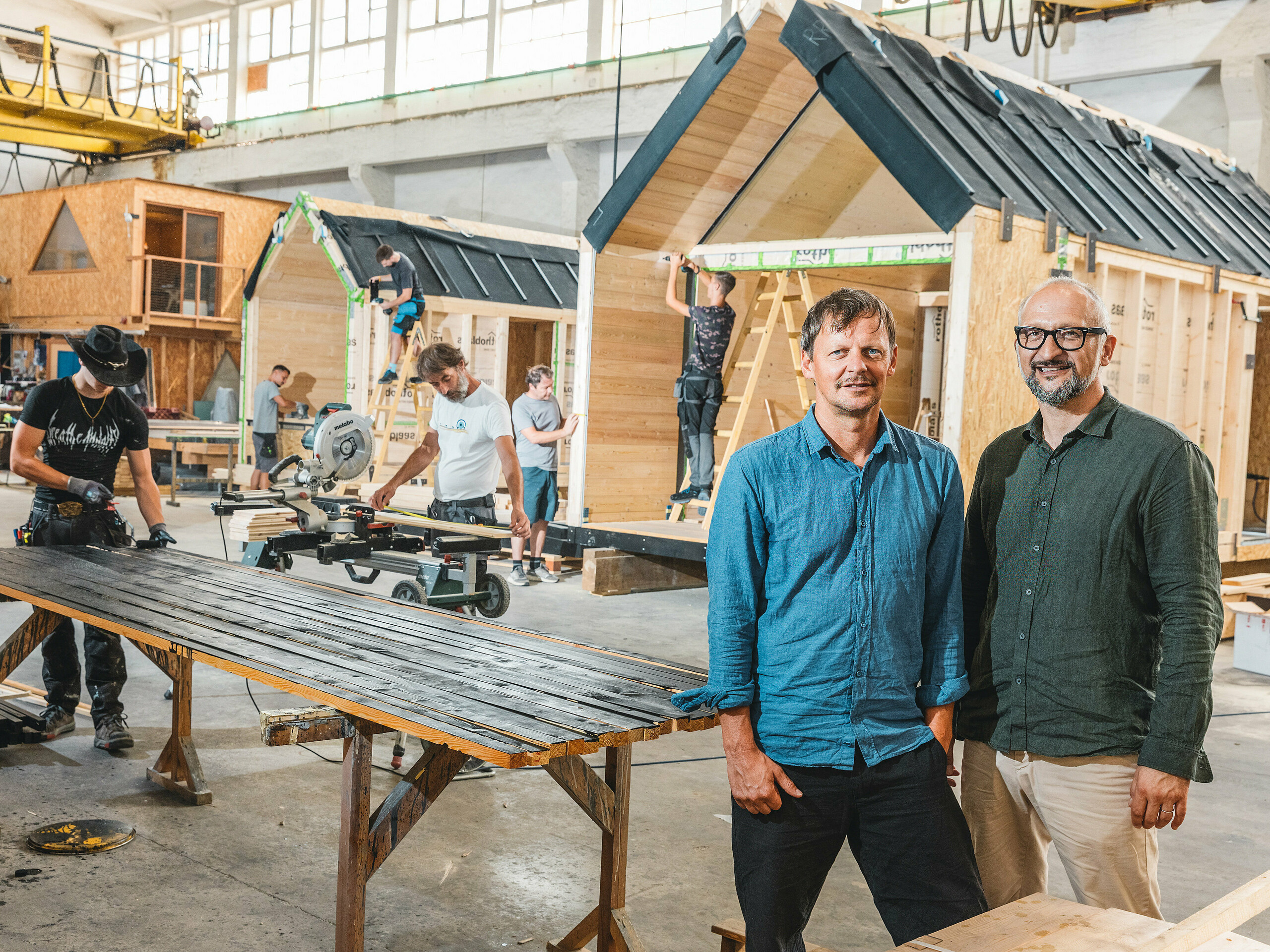 U proizvodnoj hali nastaju minimalističke tiny kuće tvrtke Lushna. Tvrtka je međunarodno uspješna i specijalizirana za miniarhitekturu u prirodnim resortima. U prvom planu nalaze se dvojica osnivača: arhitekt Peter Ličen i marketinški stručnjak Jaka Ažman.  U pozadini se montiraju A-Frame kuće. Upečatljiv kontrast drva i tamnog aluminija čini arhitekturu vizualno privlačnom, što potvrđuje i Secret Koi Garden na jezeru Natterer See.