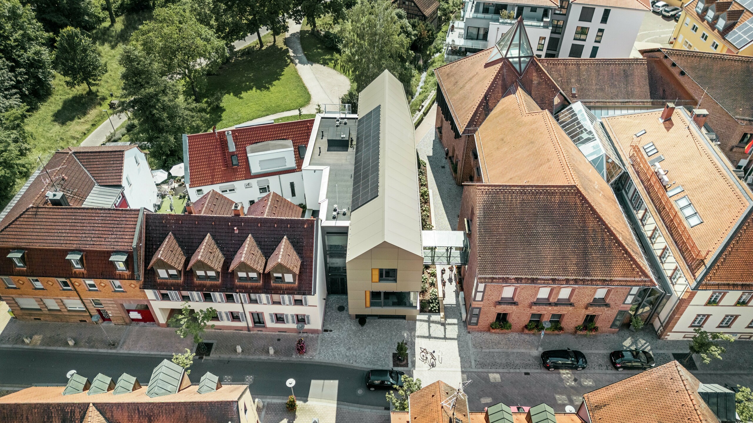 Gradska vijećnica u Alzenauu, Njemačka, nalazi se u središtu povijesnog gradskog okruženja, okružena tradicionalnim zgradama s crvenim crijepnim krovovima. U kontrastu s tim stoji moderna gradska vijećnica čija je fasada obložena aluminijskim kompozitnim pločama PREFA u elegantnoj brončanoj boji. Inovativna arhitektura jasno se izdvaja od susjednih klasičnih zgrada, a istovremeno se skladno uklapa u gradski pejzaž.