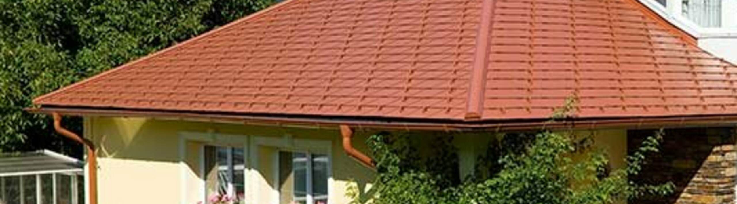 Obiteljska kuća s četverostrešnim krovom i krovnom kućicom pokrivena PREFA aluminijskom šindrom u optici crijepa, ciglasto crvenom.