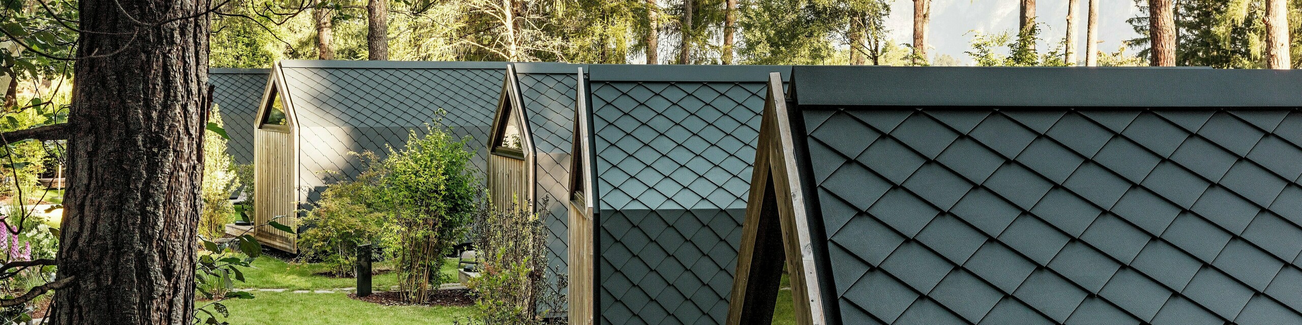 Nekoliko minimalističkih tiny kuća Secret Koi Gardena skladno je poredano duž zelene vrtne osi na jezeru Natterer See. Krovovi i fasade u potpunosti su obloženi sitnim PREFA krovnim i zidnim rombovima od aluminija u P.10 antracitnoj boji, koji stvaraju ujednačenu površinu nalik ribljoj koži.  Okružene drvećem i grmljem, trajni i vremenski otporni PREFA aluminijski proizvodi precizno spajaju arhitekturu s mirom, prirodom i visokokvalitetnim glamping dizajnom.