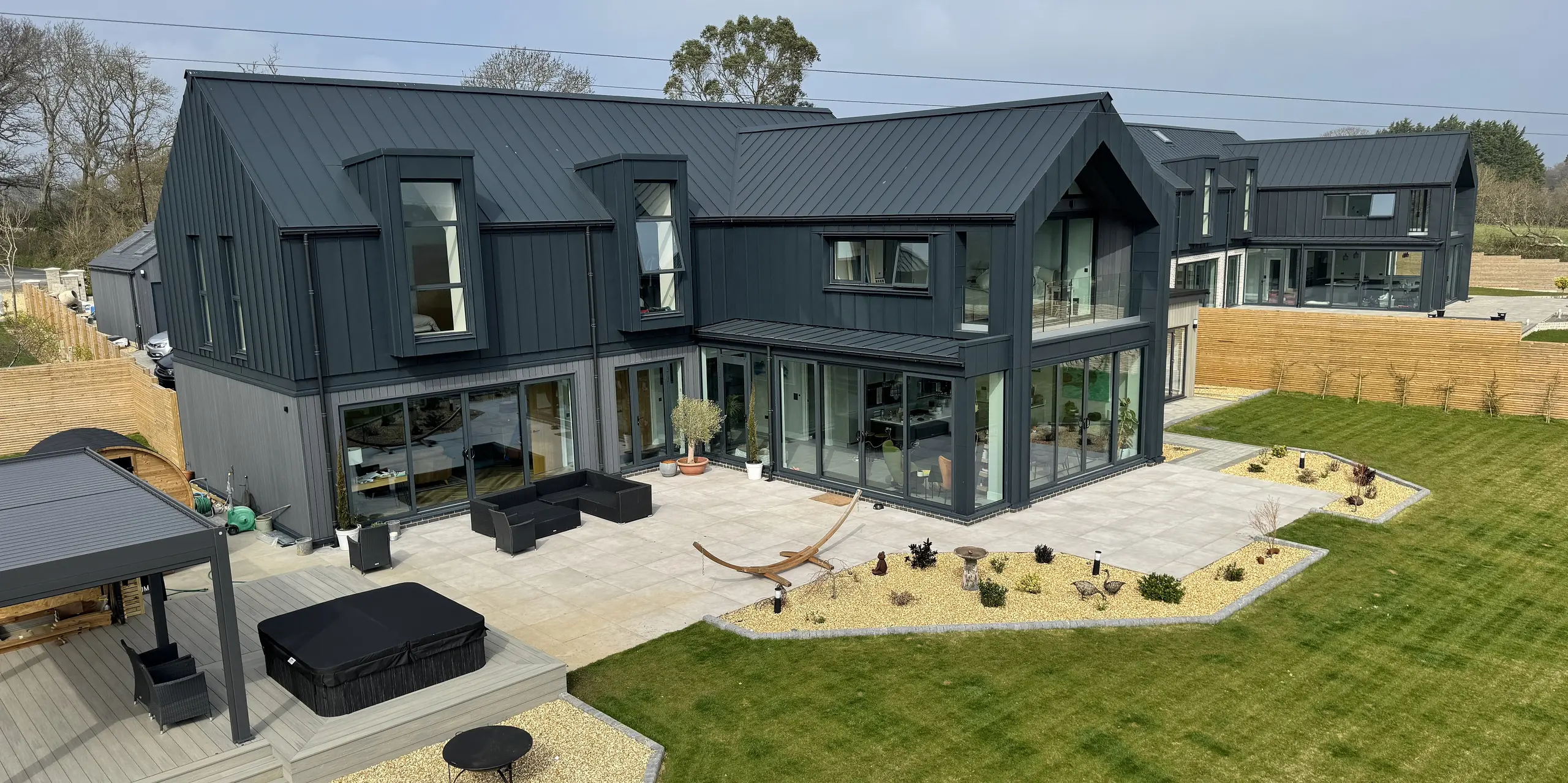Zwei moderne Einfamilienhäuser auf der Isle of Wight mit markanter PREFALZ Dach- und Fassadenverkleidung in P.10 Dunkelgrau. Die klare Linienführung und die großzügigen Glasfronten schaffen ein lichtdurchflutetes Ambiente. Die Aluminiumoberflächen sind korrosionsbeständig, langlebig und wartungsarm – ideal für die Küstenlage. Unterschiedliche Materialien im Erdgeschoss setzen subtile Akzente und verleihen dem Ensemble Individualität. Die Kombination aus zeitgemäßer Architektur und hochwertigen PREFA Produkten macht dieses Projekt zu einem echten Eyecatcher.