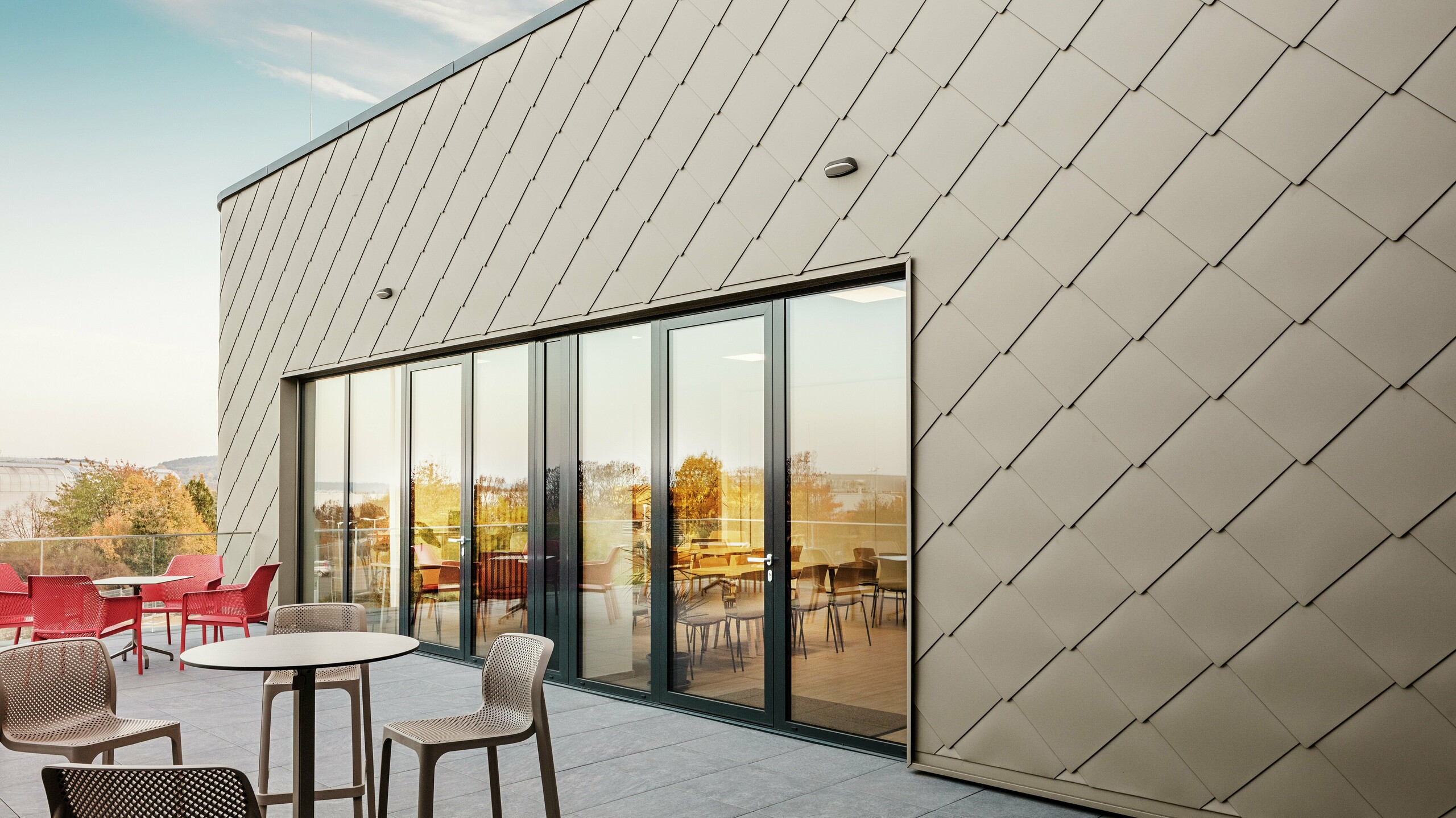 Die Fassade des neuen PREFA Standortes in Törökbálint besticht durch die eleganten PREFA Wandrauten 44 × 44 in Bronze. Die präzise verlegte Aluminiumfassade sorgt für ein modernes, dynamisches Erscheinungsbild und bietet gleichzeitig maximalen Schutz vor Witterungseinflüssen. Die großzügige Glasfront verbindet Innen- und Außenbereich und schafft auf der großzügigen Terrasse eine helle und einladende Atmosphäre.