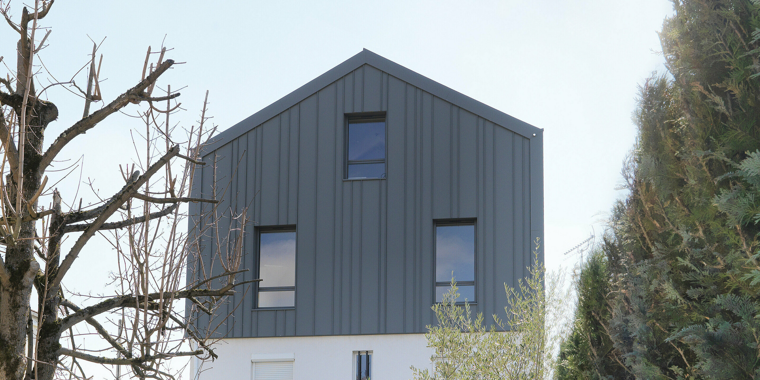 Blick vom Garten auf ein Einfamilienhaus in Houilles (Frankreich). Für das Gebäude wurden PREFA Sidings in P.10 Reinweiss an der Fassade und PREFALZ in P.10 Hellgrau an Dach und Fassade kombiniert.