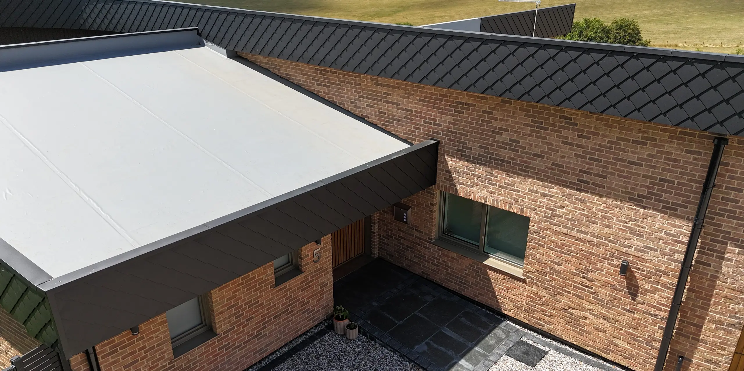 Dieses moderne Einfamilienhaus besticht durch seine markante Eingangsüberdachung sowie die elegante Kombination aus Klinkerfassade und PREFA Wandraute 20 × 20 in Anthrazit. Die langlebigen Blechrauten setzen klare Akzente und unterstreichen die hochwertige Architektur. Dank der robusten PREFA-Aluminiumprodukte ist die Fassade witterungsbeständig und pflegeleicht. Die Verbindung natürlicher Materialien mit modernen Aluminiumlösungen macht dieses Objekt zu einem Eyecatcher für nachhaltiges und stilvolles Wohnen.