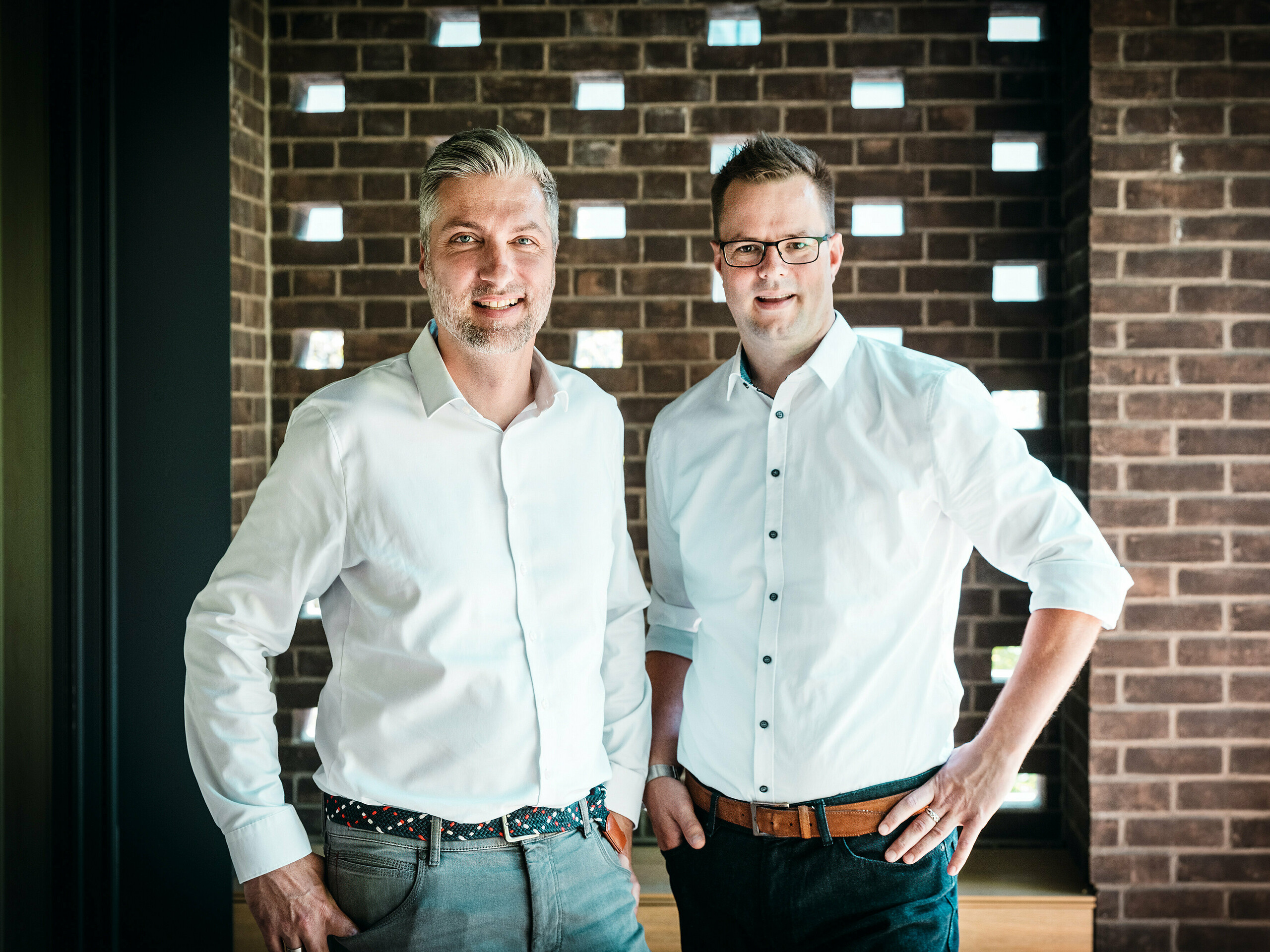 Arhitektonski tim A Fiúk Építész Stúdió stoji u modernom interijeru budimpeštanske višegeneracijske vile, koja je nagrađena u okviru PREFARENZEN 2026. Ispred karakterističnog zida od opeke predstavljaju precizan jezik materijala i formi svog projekta, koji je obilježen kubičnim PREFALZ aluminijskim krovom u boji P.10 antracit. Scena naglašava arhitektonsku stručnost, visokokvalitetnu izvedbu i svjestan odabir materijala, pri čemu PREFA aluminij uvjerava svojom dugotrajnošću, snažnim dizajnom i tehničkom preciznošću.