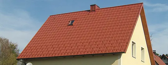 Klasični dvostrešni krov s malim krovnim prozorom i dimnjakom, pokriven PREFA krovnom pločom u ciglasto crvenoj sa snjegobranima i sigurnosnim krovnim kukama.