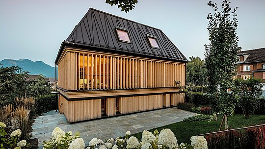 Moderno „Badehaus“ hotela Hirschen u Schwarzenbergu ima nagrađivani PREFA krov s falcom u boji P.10 orah smeđa. Ikonični krov s četiri vode, nagiba 60 stupnjeva i nekonvencionalno postavljenim falcima, predstavlja arhitektonsko remek-djelo koje spaja tradiciju i inovaciju. Fasada od vertikalnih drvenih lamela daje zgradi toplu, prirodnu pojavu i skladno se uklapa u zaštićeno središte mjesta. PREFALZ oduševljava dugovječnošću, slobodom oblikovanja i izvrsnom obradivošću, čak i kod složenih krovnih oblika. Nagrađivani primjer inovativne arhitekture s visokokvalitetnim PREFA proizvodima.