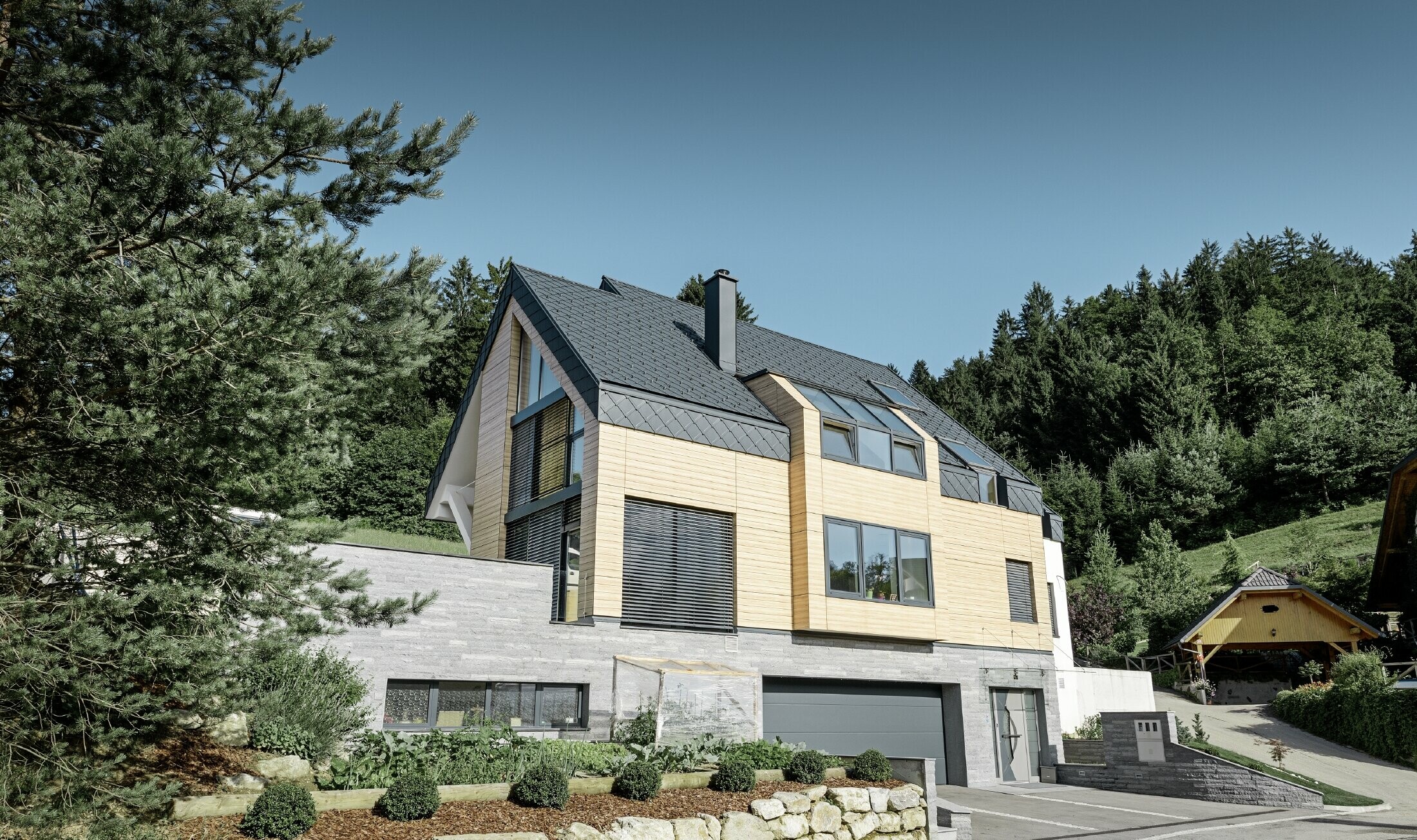 Obiteljska kuća s dvostrešnim krovom bez nadstrešnice s fasadom u optici drva i aluminijskim krovom u antracit boji