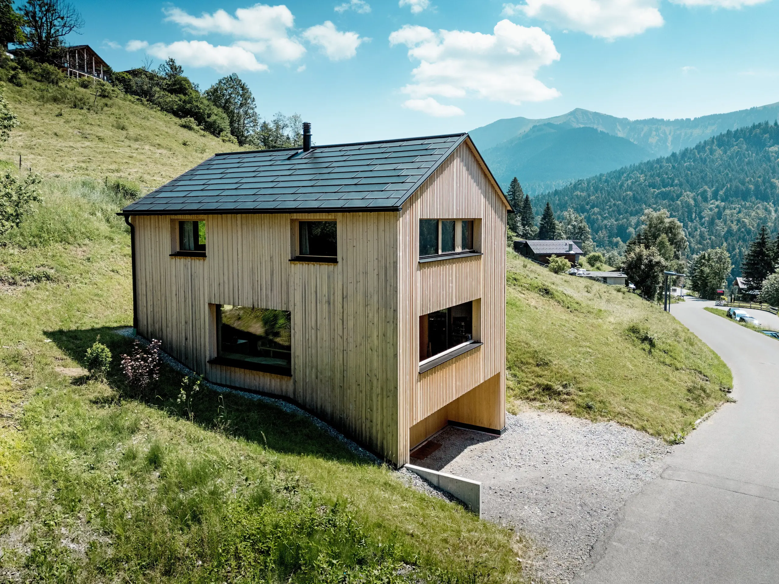 Visoko iznad doline kuća Immi stoji poput jasnog drvenog monolita na osunčanoj padini planinskog naselja Ebnit. Svedena fasada od bijele jele i crni PREFA solarni krov stvaraju snažan kontrast prostranom alpskom krajoliku. Integrirane solarne krovne ploče i krovne ploče R.16 u boji P.10 Crna proizvode električnu energiju iz sunca, odolijevaju zahtjevnim alpskim vremenskim uvjetima te osiguravaju dugotrajan i skladan izgled krova.